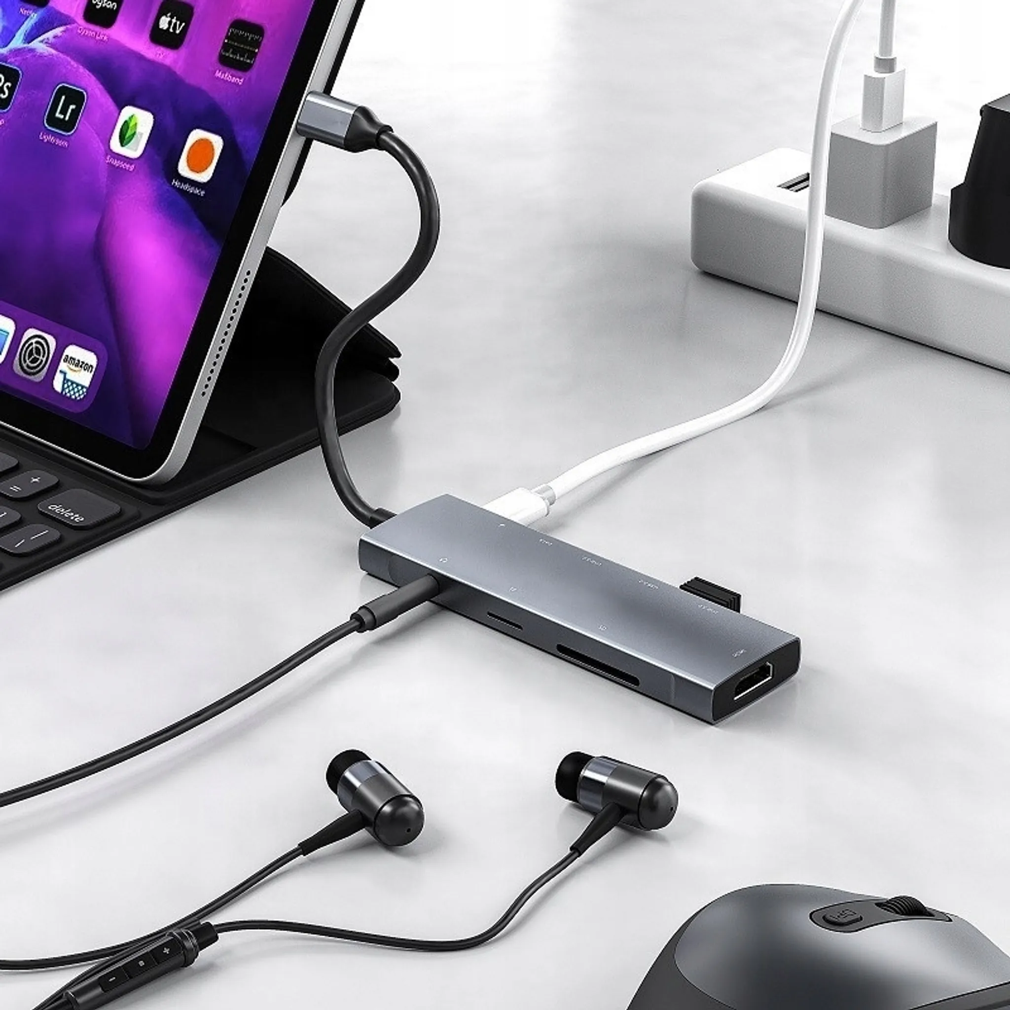 Ein grauer USB-C-Hub mit mehreren Anschlüssen, verbunden mit einem Tablet, Kopfhörern und einer Maus, auf einem Schreibtisch.