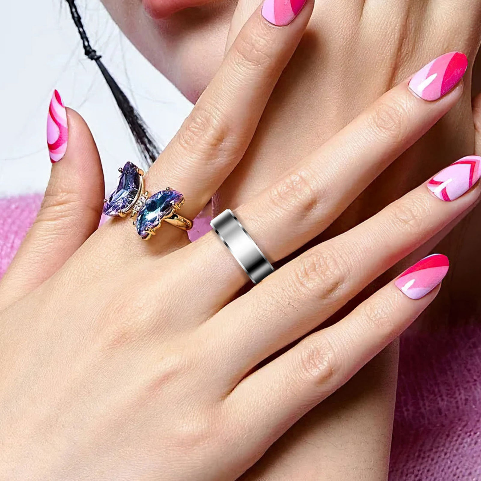 Hand einer Frau mit silbernem Ring. Eine andere Hand mit einem Schmetterlingsring. Rosa Nagellack.