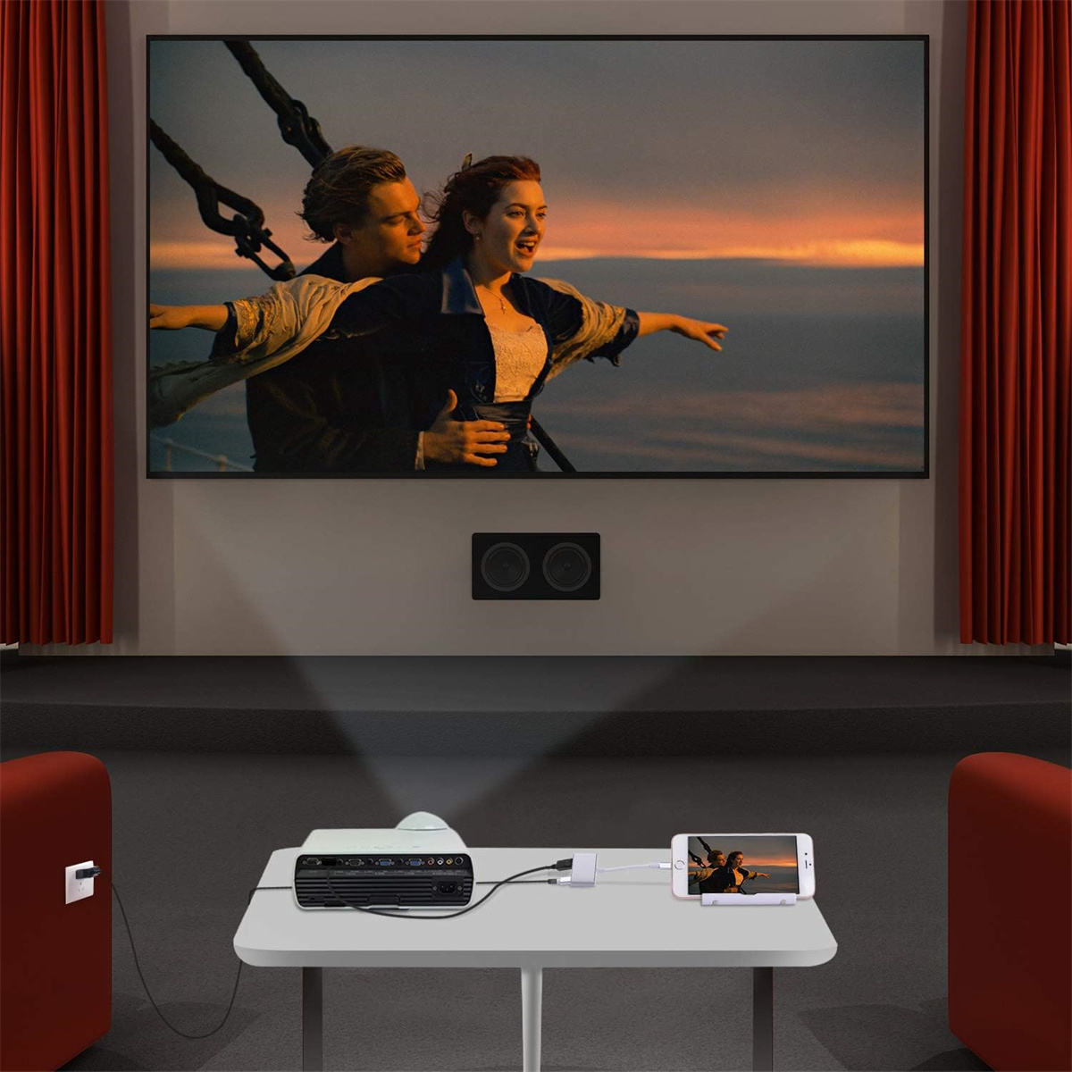 Eine Filmszene, die auf einer Leinwand mit einem Projektor, einem Tisch und roten Stühlen abgespielt wird.
