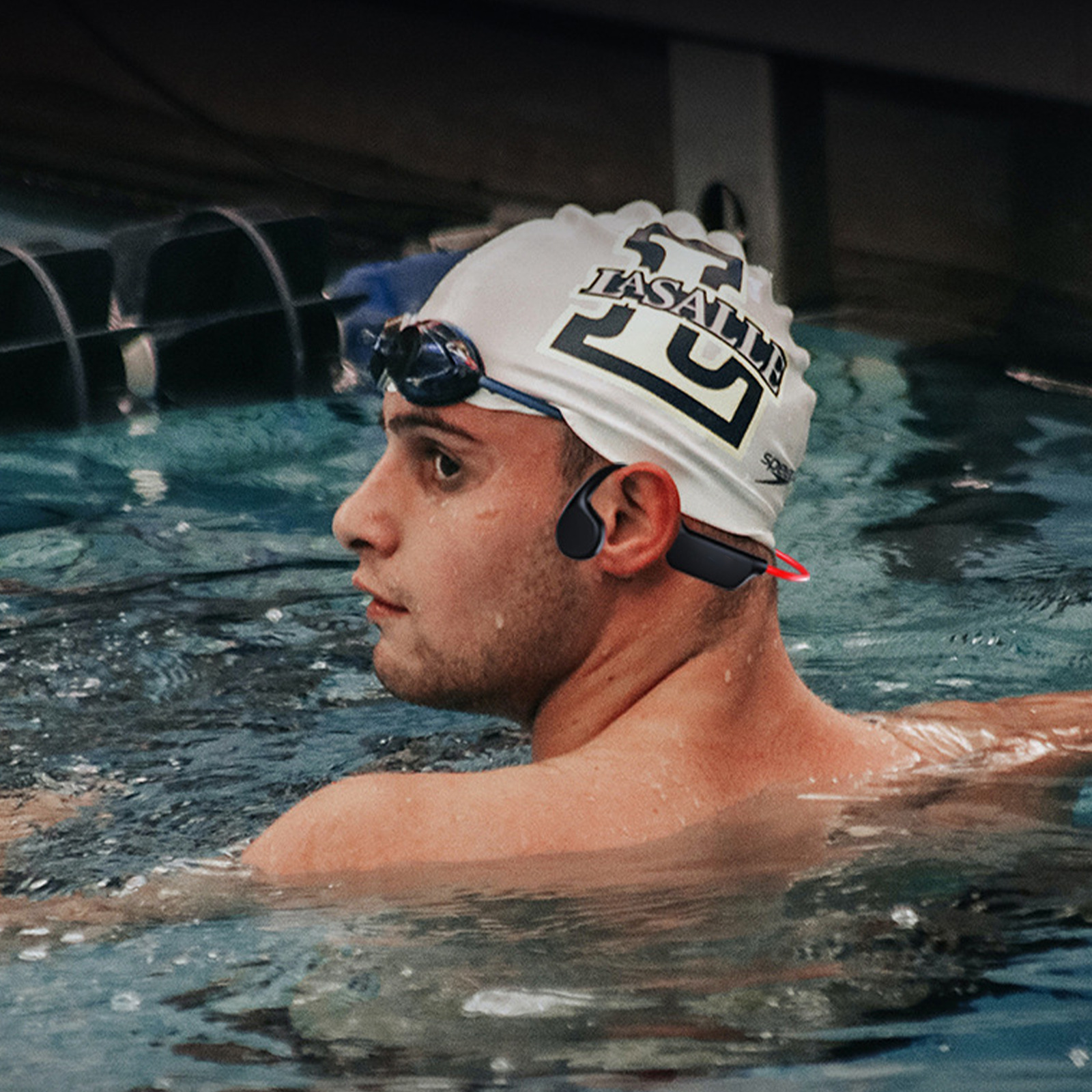 Ein Mann mit Schwimmbrille und Badekappe in einem Pool, der einen schwarzen Kopfhörer trägt.