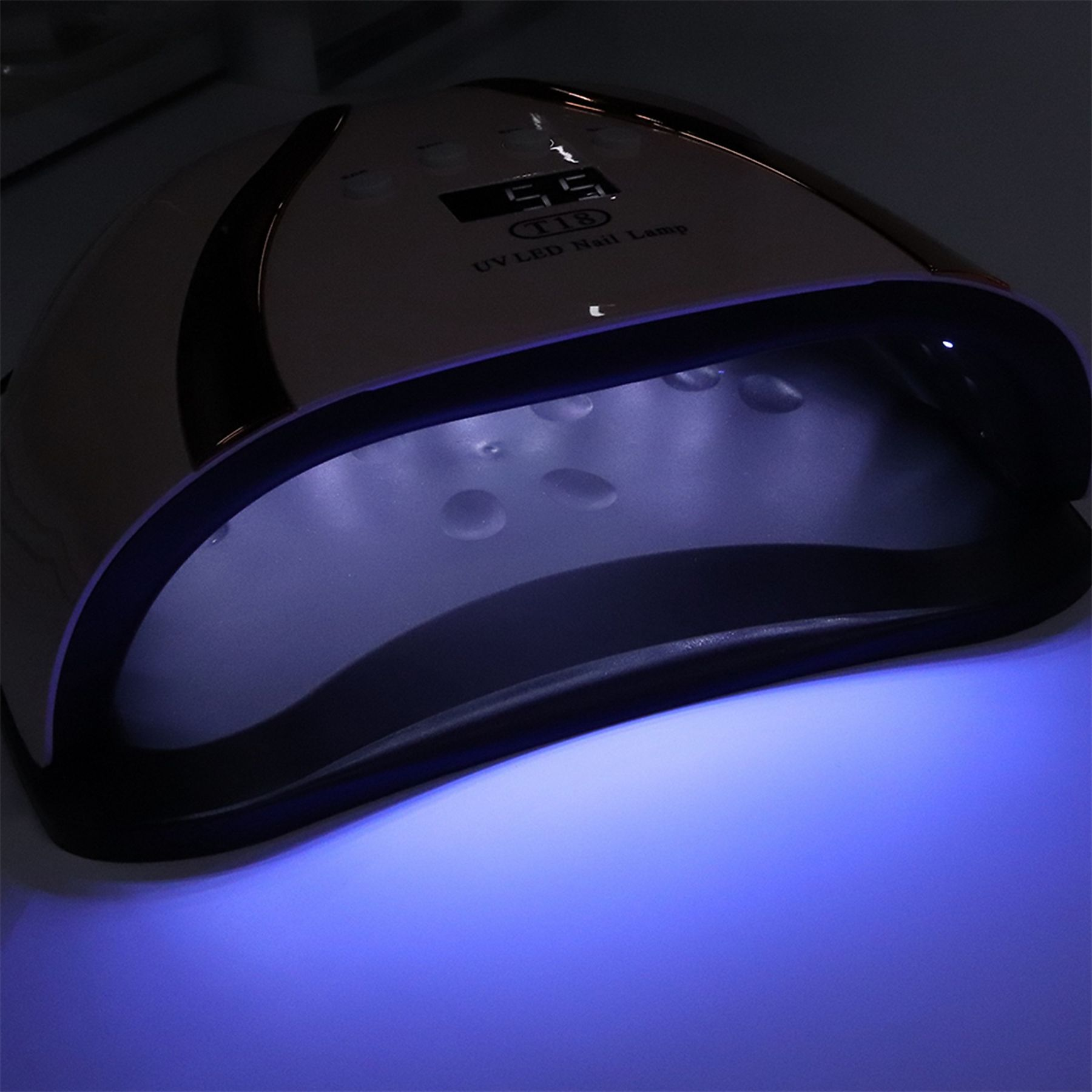 Eine Nagellampe mit rosa-weißem Finish wird gezeigt, wobei blaues Licht von innen ausgeht. Die Lampe ist an.