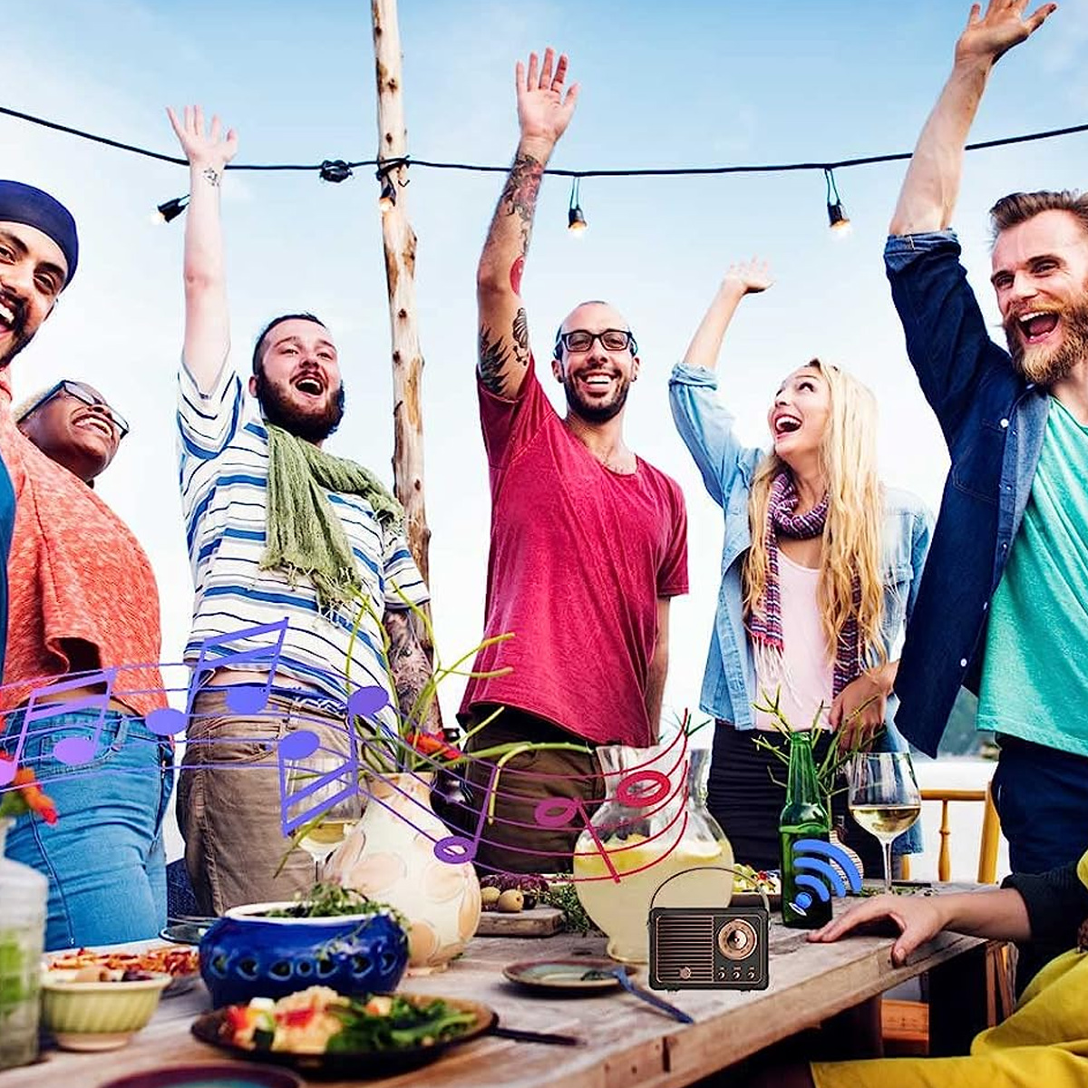 Gruppe von Leuten feiert draußen. Sie heben die Arme. Ein Tisch mit Essen und einem Radio ist im Vordergrund.