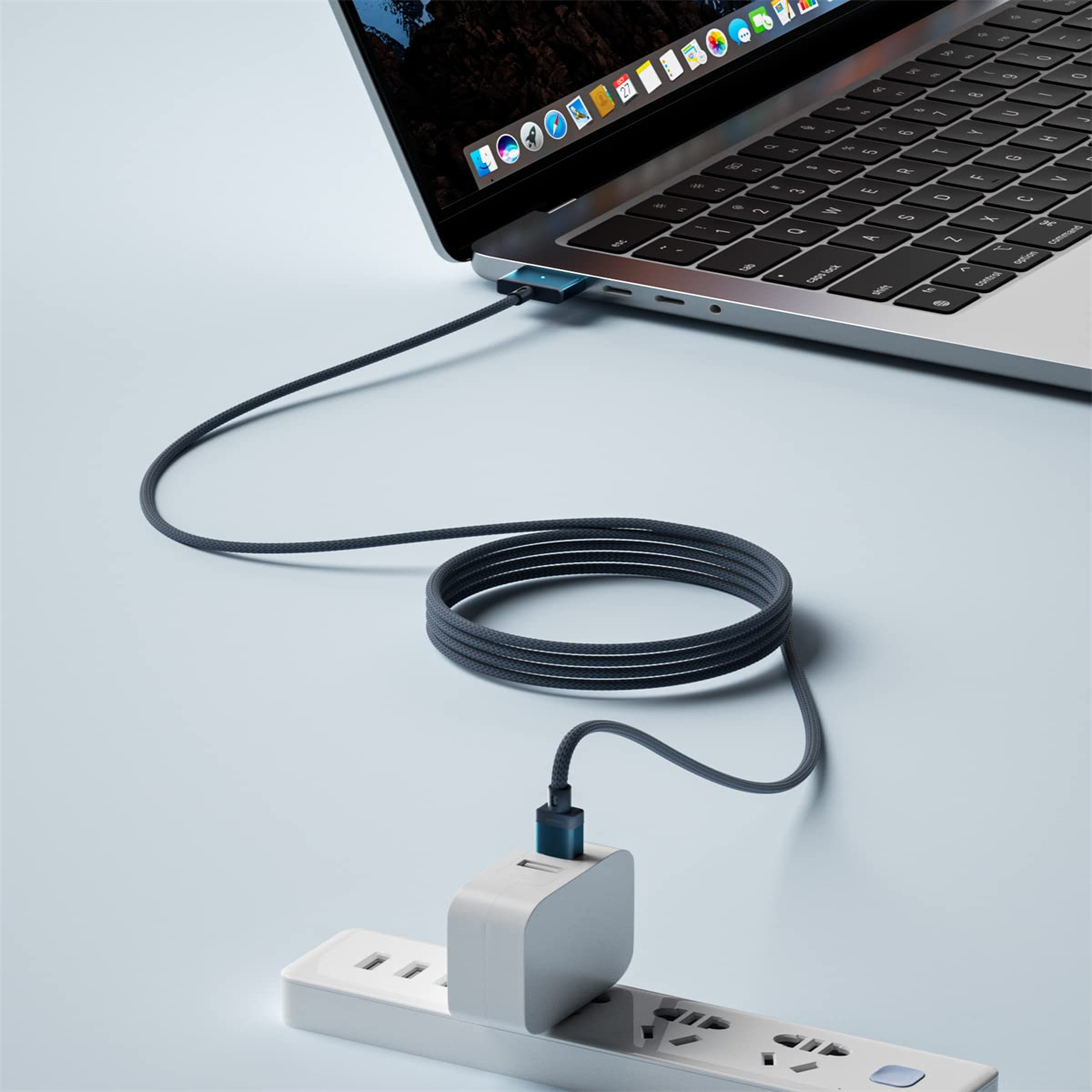 Laptop, der über ein Ladekabel an eine Steckdosenleiste angeschlossen ist. Graues Kabel.