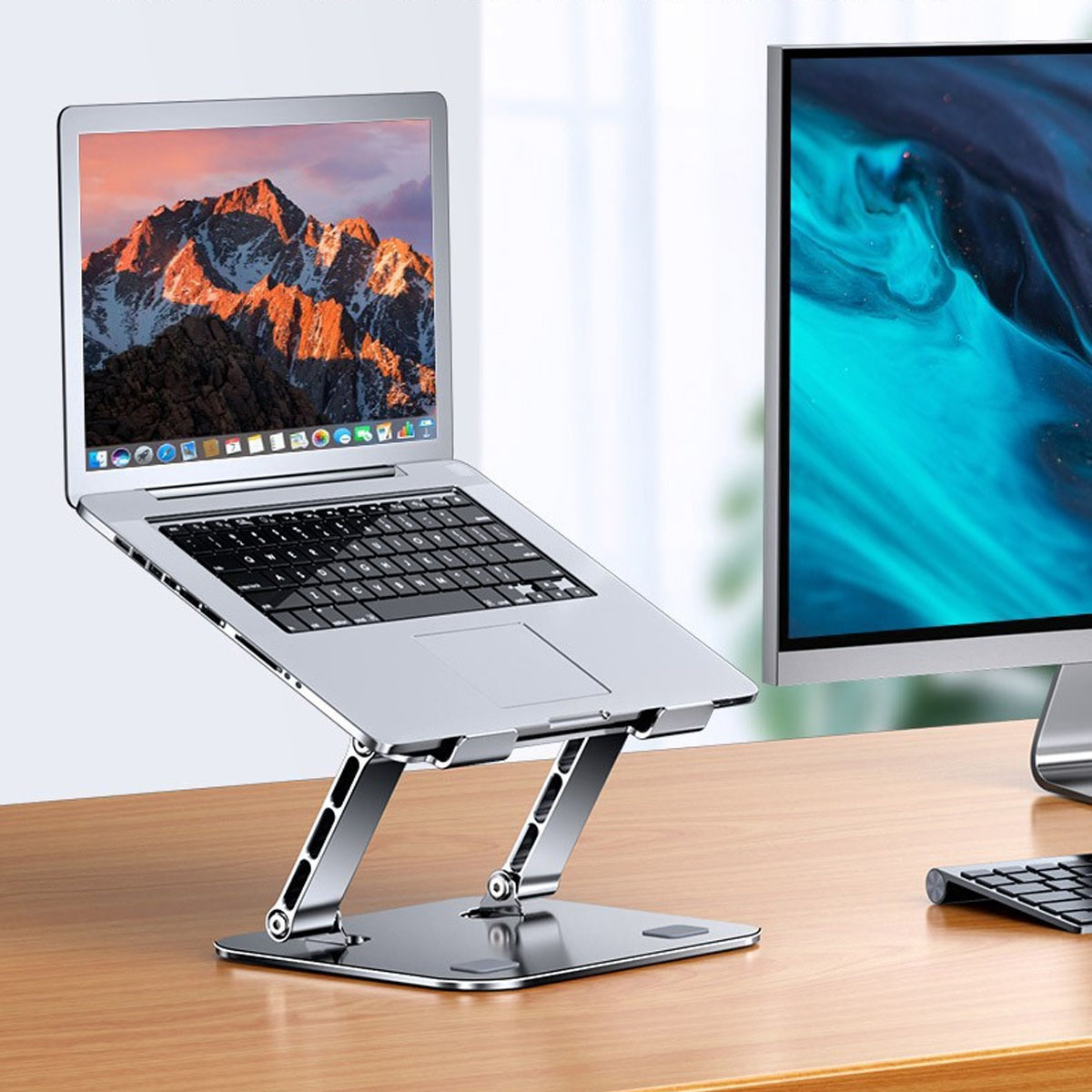 Laptop auf einem Ständer mit einem externen Monitor und einer Tastatur auf einem Holzschreibtisch.