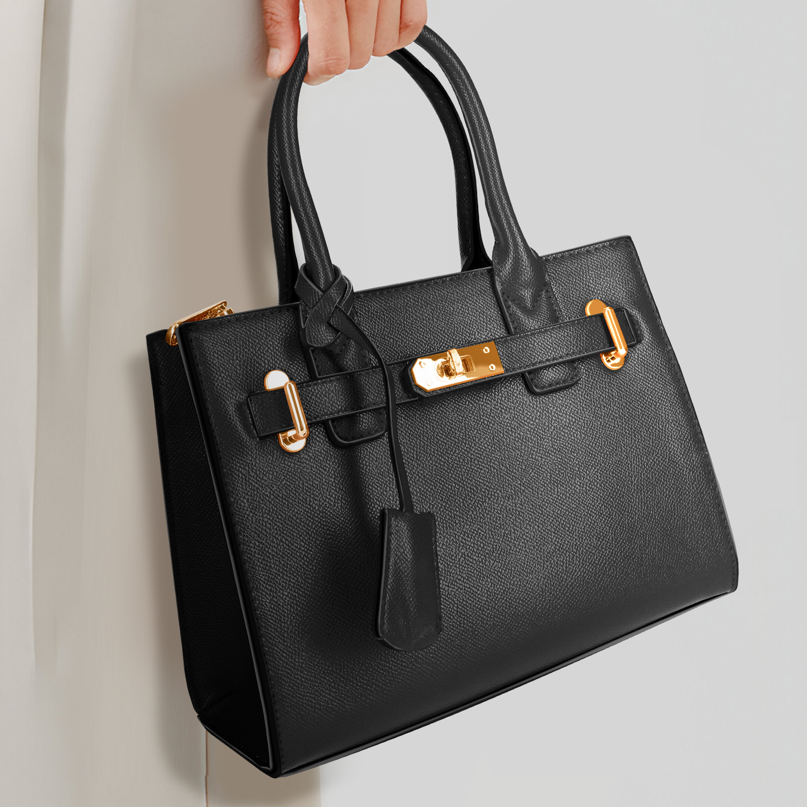 Schwarze Lederhandtasche mit goldfarbener Hardware, gehalten von einer Hand, weißer Hintergrund.