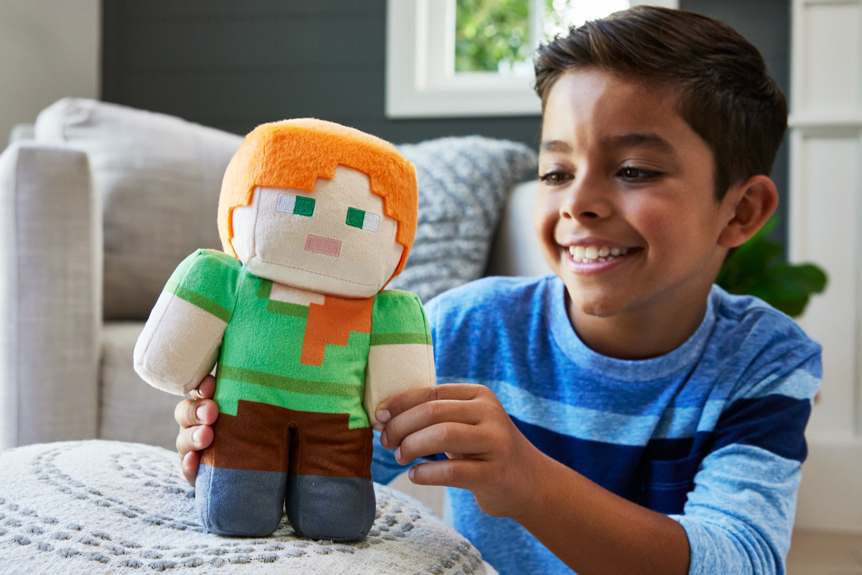 Ein Junge lächelt, während er ein Minecraft Alex Stofftier hält, das ein grünes Hemd und eine braune Hose trägt.