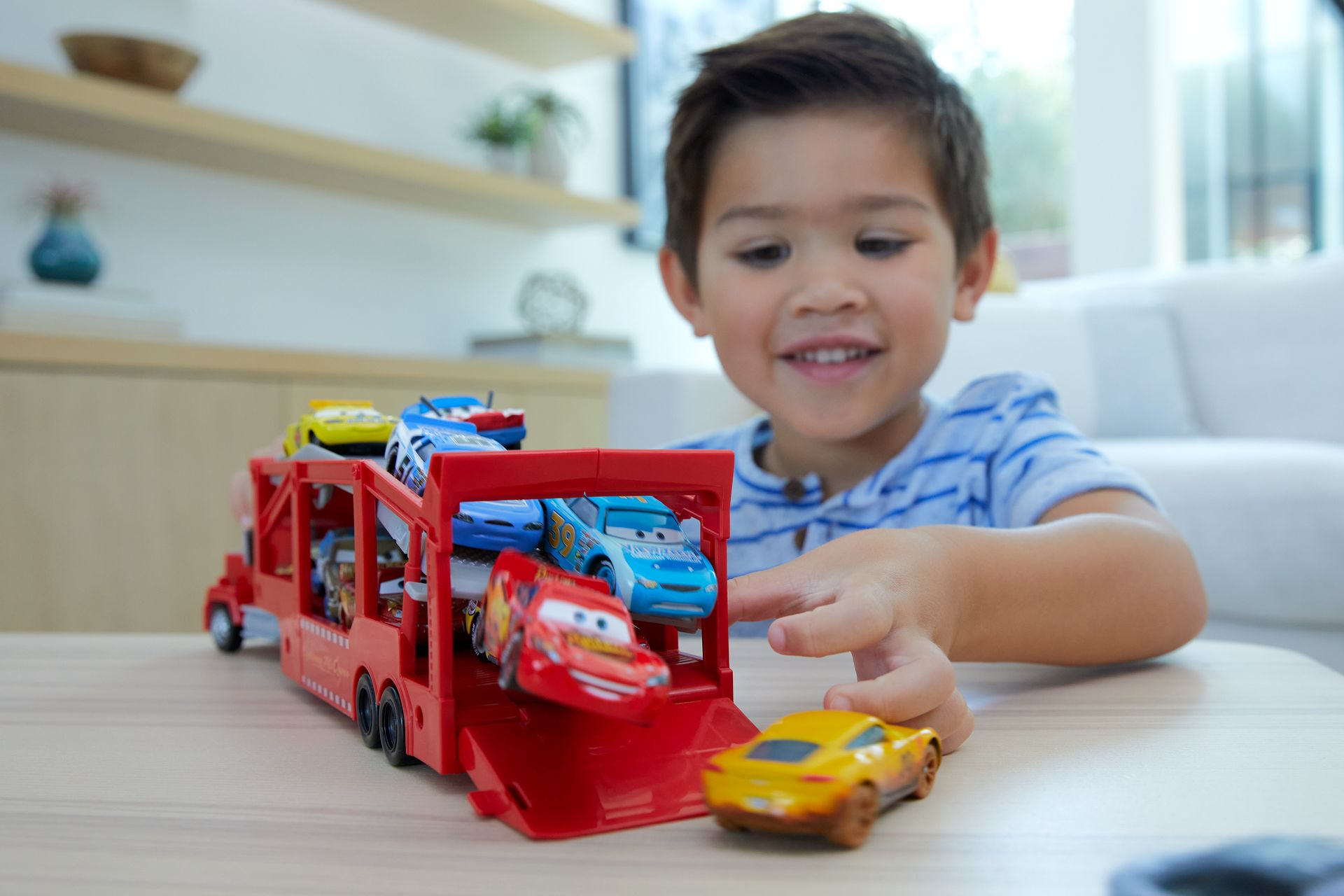 Junge spielt mit Spielzeugautos. Roter LKW, verschiedene Spielzeugautos. Lachendes Kind drinnen.