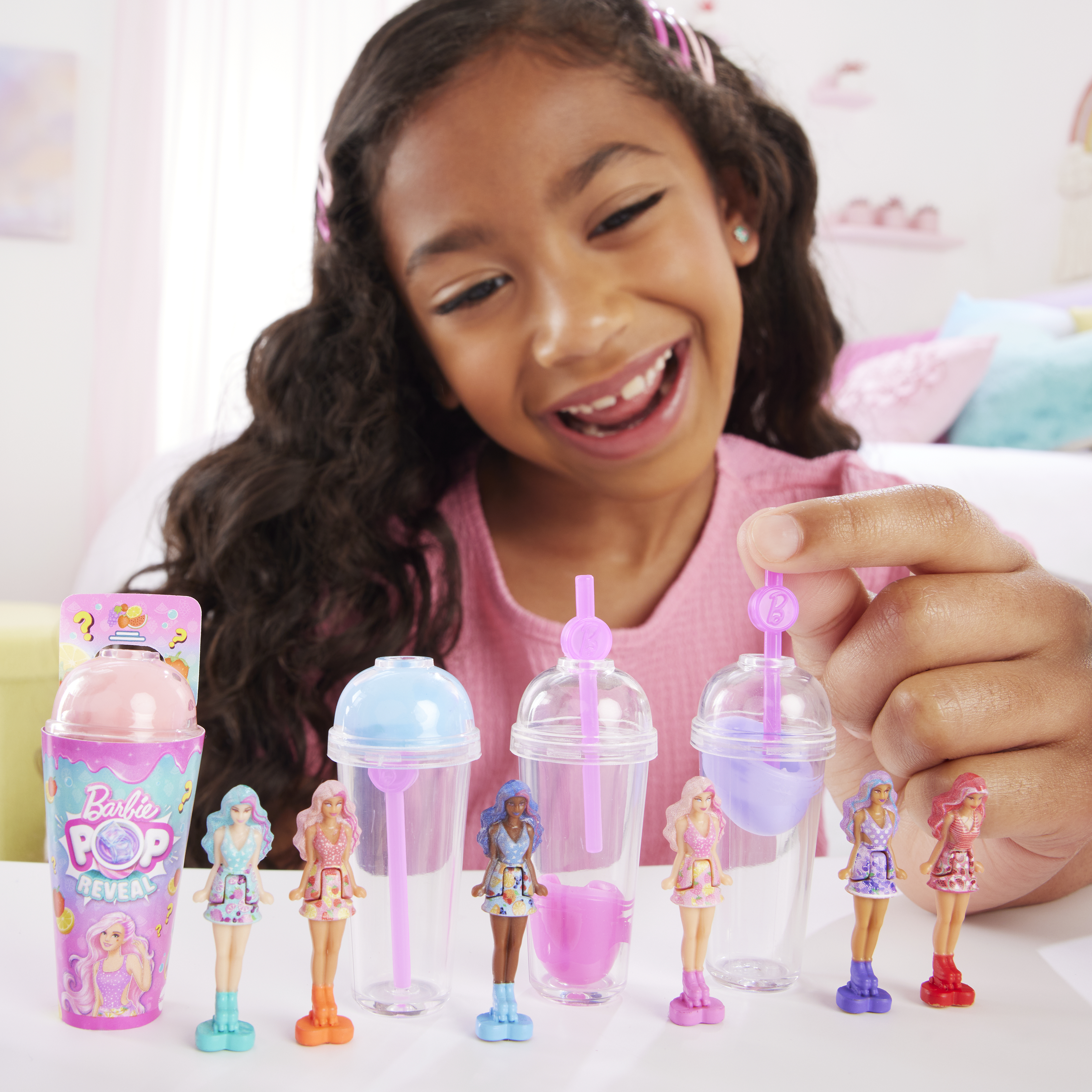 Ragazza sorridente, guarda le bambole Barbie Color Reveal nelle tazze. Sfondo rosa.