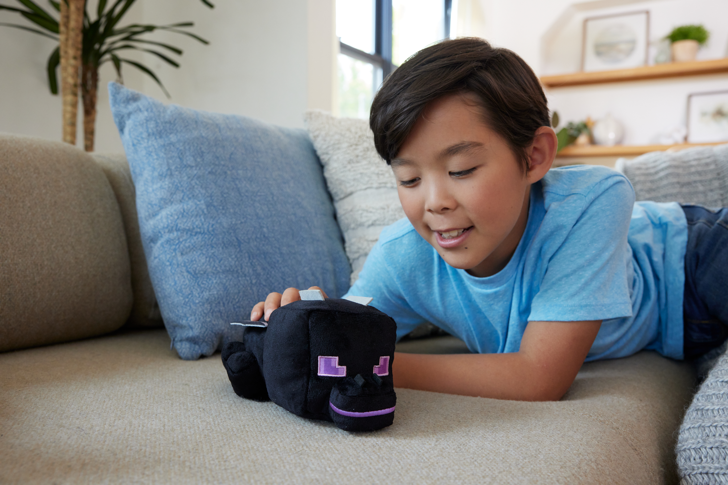 Un niño mirando un peluche de Enderman negro en un sofá. El juguete tiene ojos morados.
