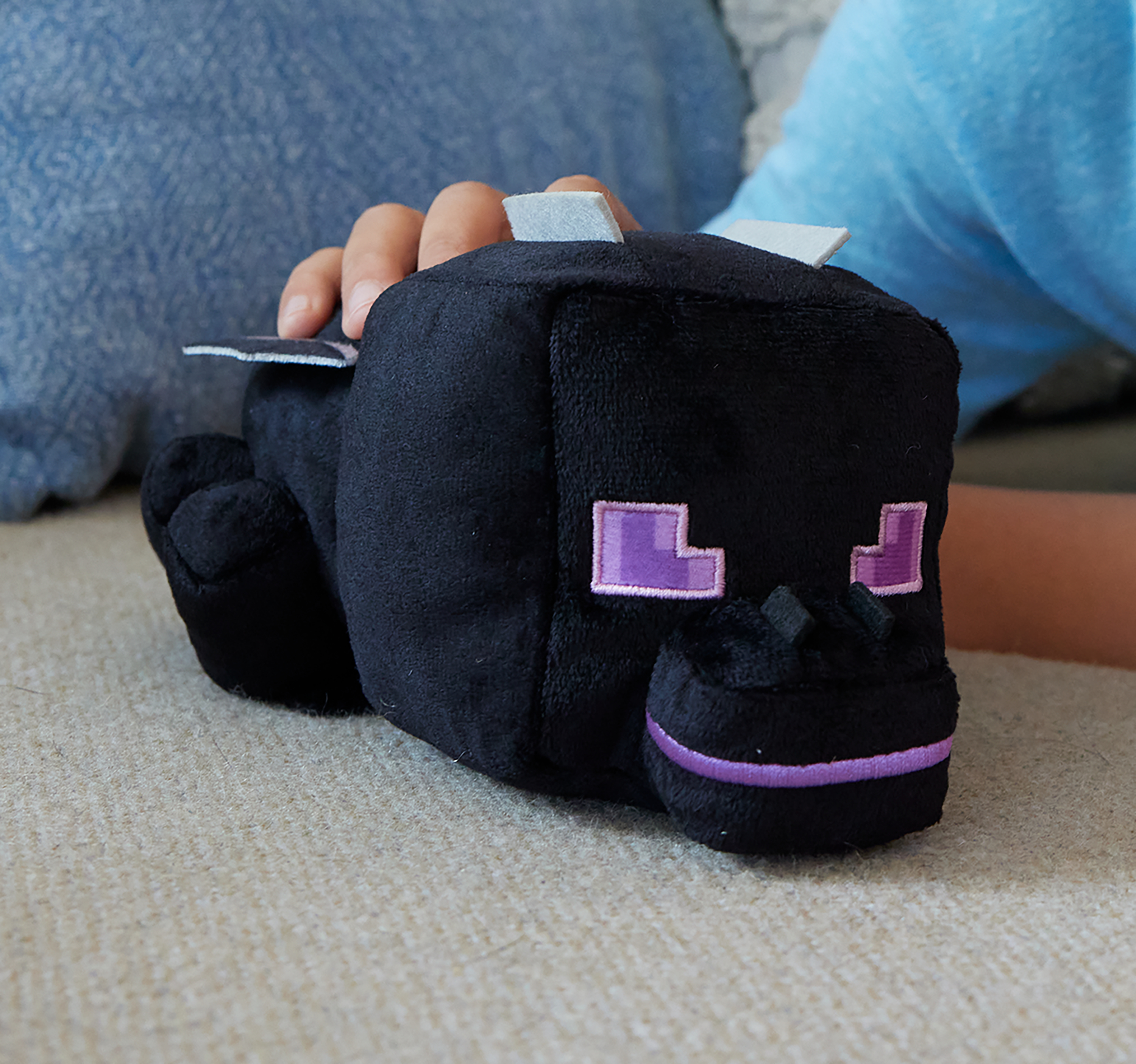 Se muestra un peluche Enderman de Minecraft negro, sostenido por una persona. Tiene ojos y detalles de boca morados.