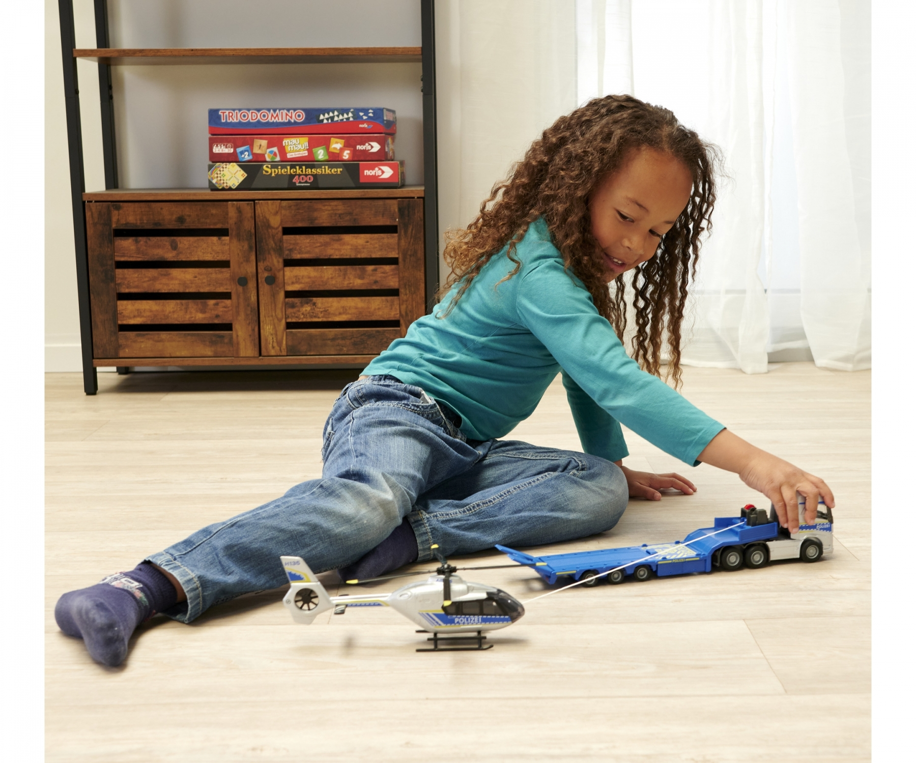 Dziewczynka bawiąca się zabawką ciężarówką i helikopterem na podłodze.