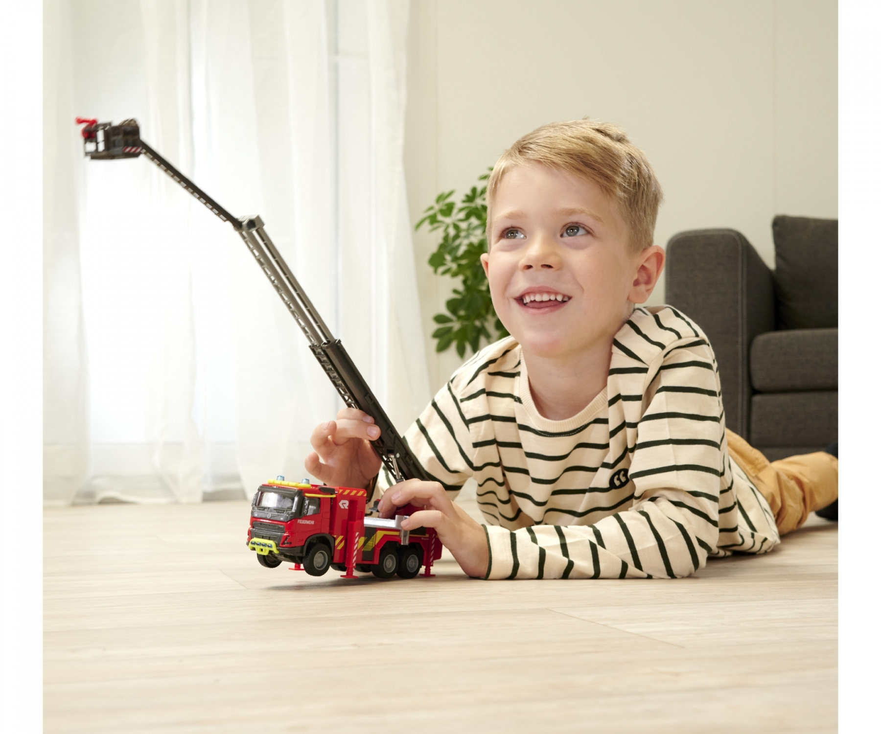 Chłopiec bawiący się czerwoną zabawką wóz strażacki, uśmiechnięty, na drewnianej podłodze.