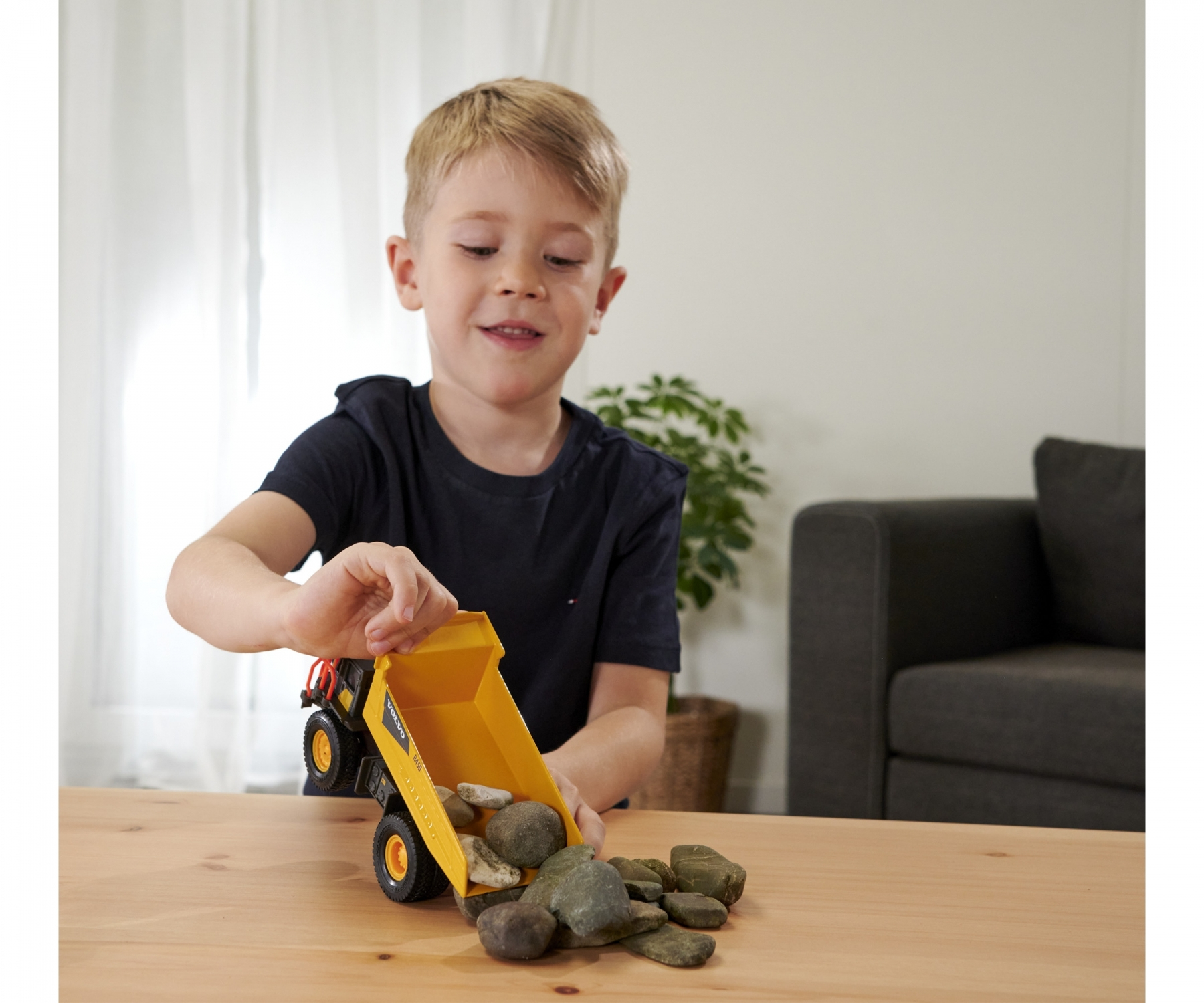 Chłopiec w ciemnej koszulce bawi się zabawną wywrotką wypełnioną kamieniami, uśmiechając się.