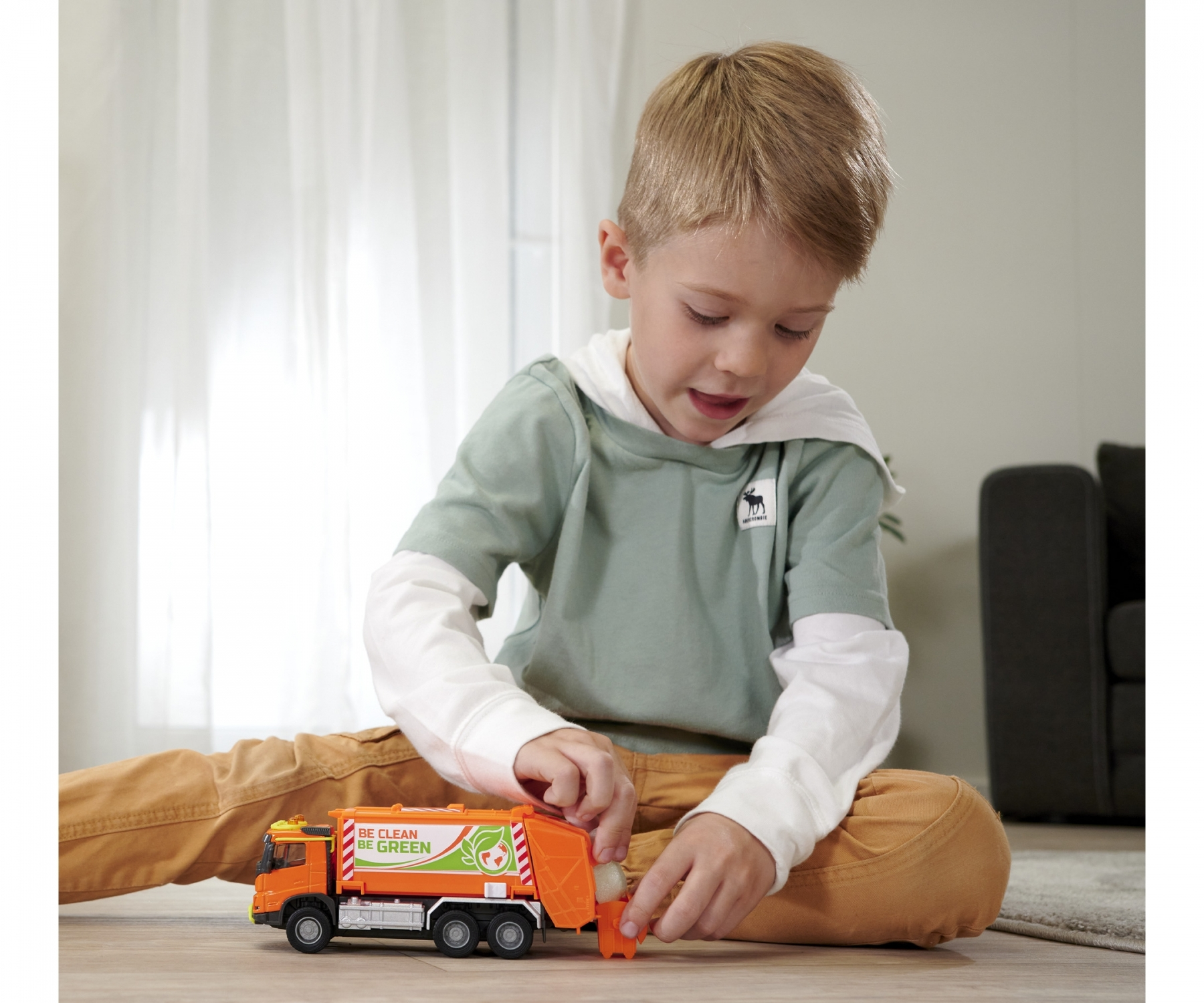 Mały chłopiec bawi się zabawkową śmieciarką. Ciężarówka jest pomarańczowa.