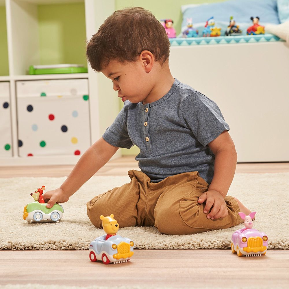 Ein kleiner Junge spielt mit Spielzeugautos auf einem Teppich. Drei Spielzeugautos sind im Vordergrund sichtbar.