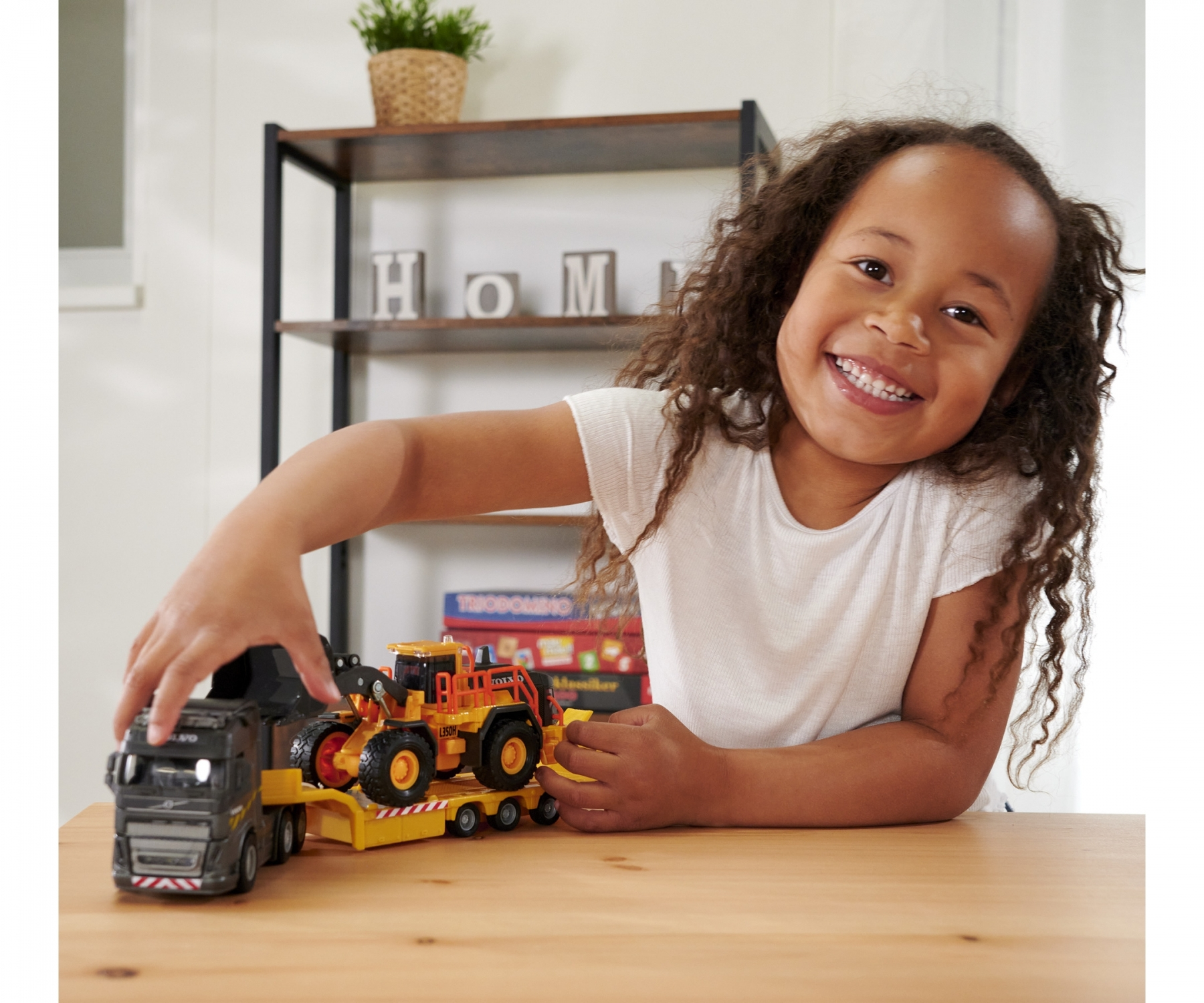Dziewczynka bawi się zabawkami ciężarówkami. Jedna ciężarówka jest na przyczepie.