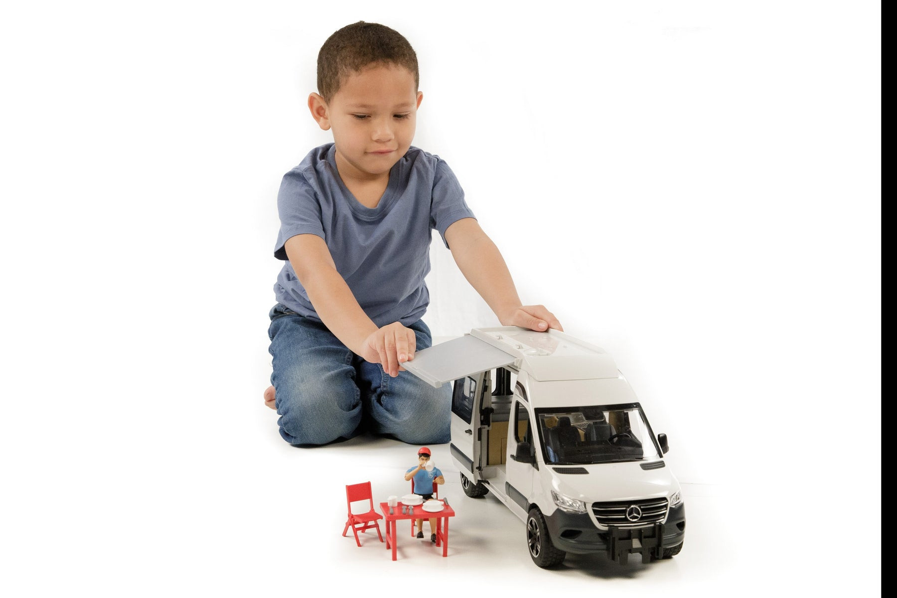 Chłopiec bawiący się zabawką furgonetką z czerwonym stołem i krzesłami na zewnątrz.
