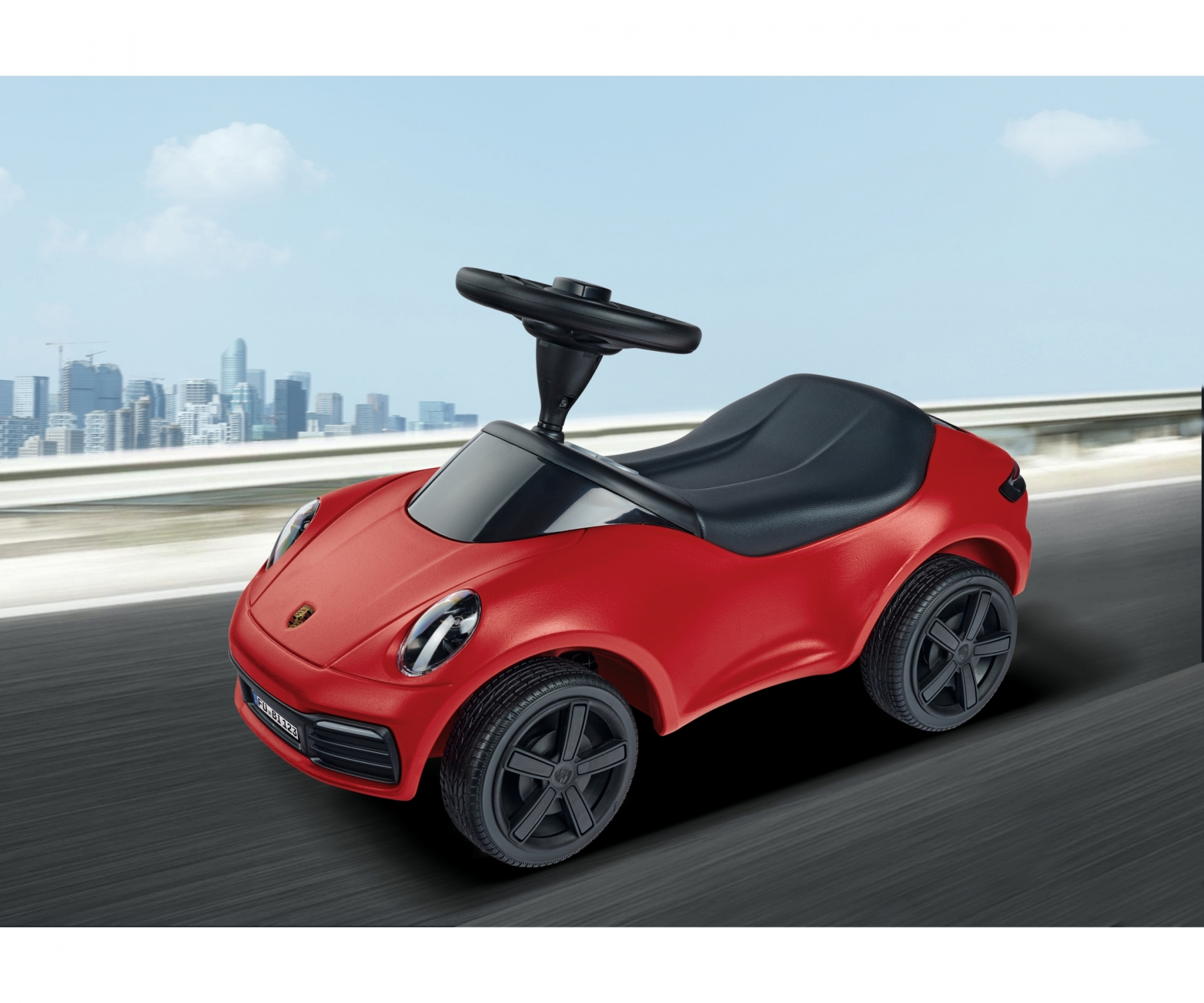 Ein rotes Spielzeug-Porsche-Auto mit schwarzen Rädern und einem schwarzen Sitz befindet sich auf einer Oberfläche mit einer Stadtlandschaft im Hintergrund.