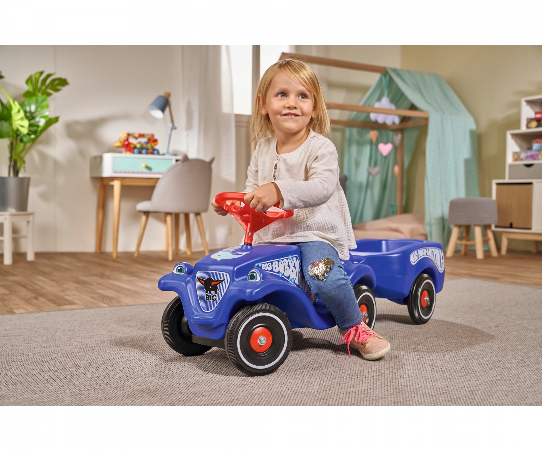 Ein kleines Mädchen fährt ein blaues Spielzeugauto. Sie lächelt.