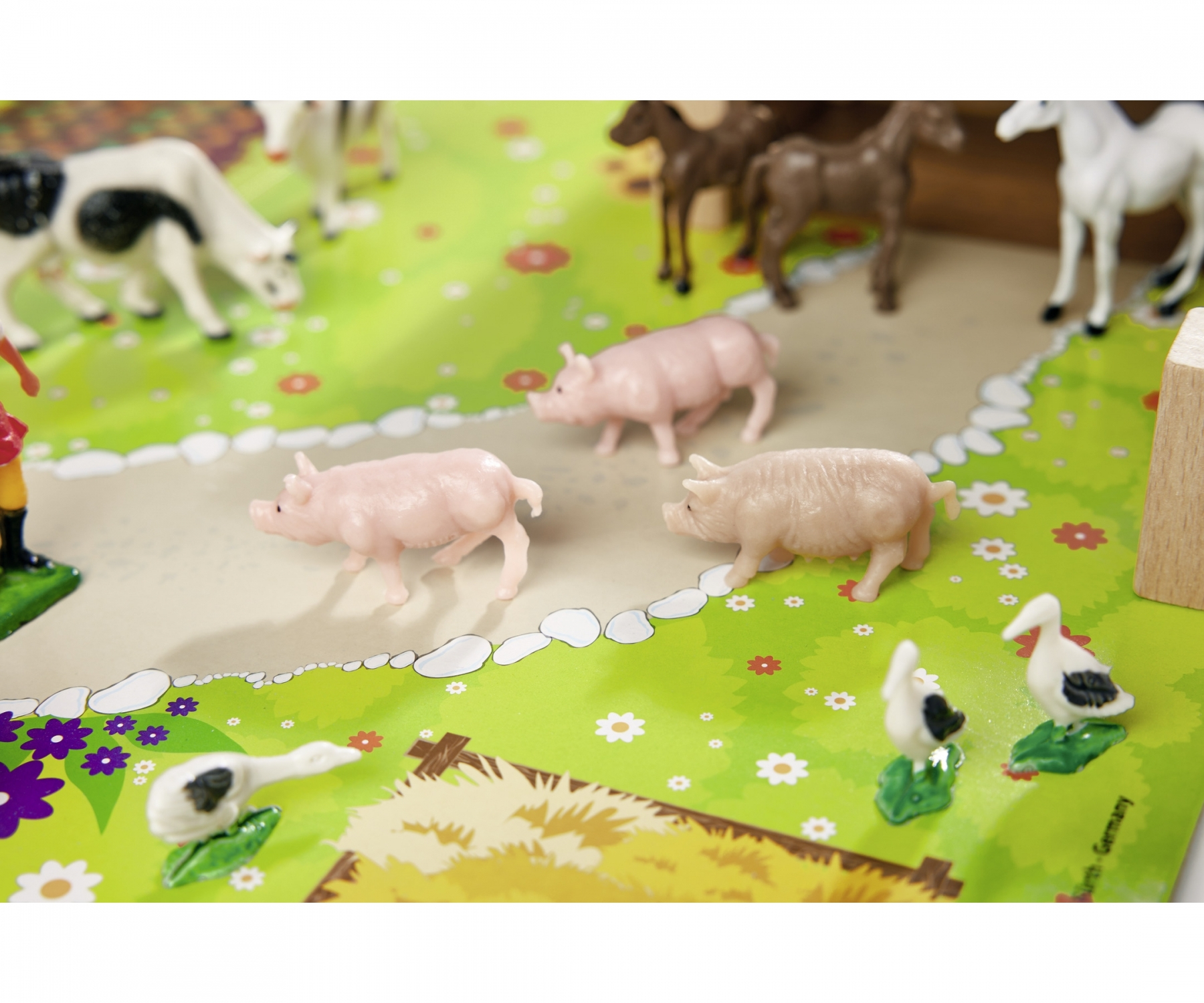 Scena z gospodarstwa zabawkowego z świniami, krowami i kaczkami na zielono-białej powierzchni, z drewnianym tłem.