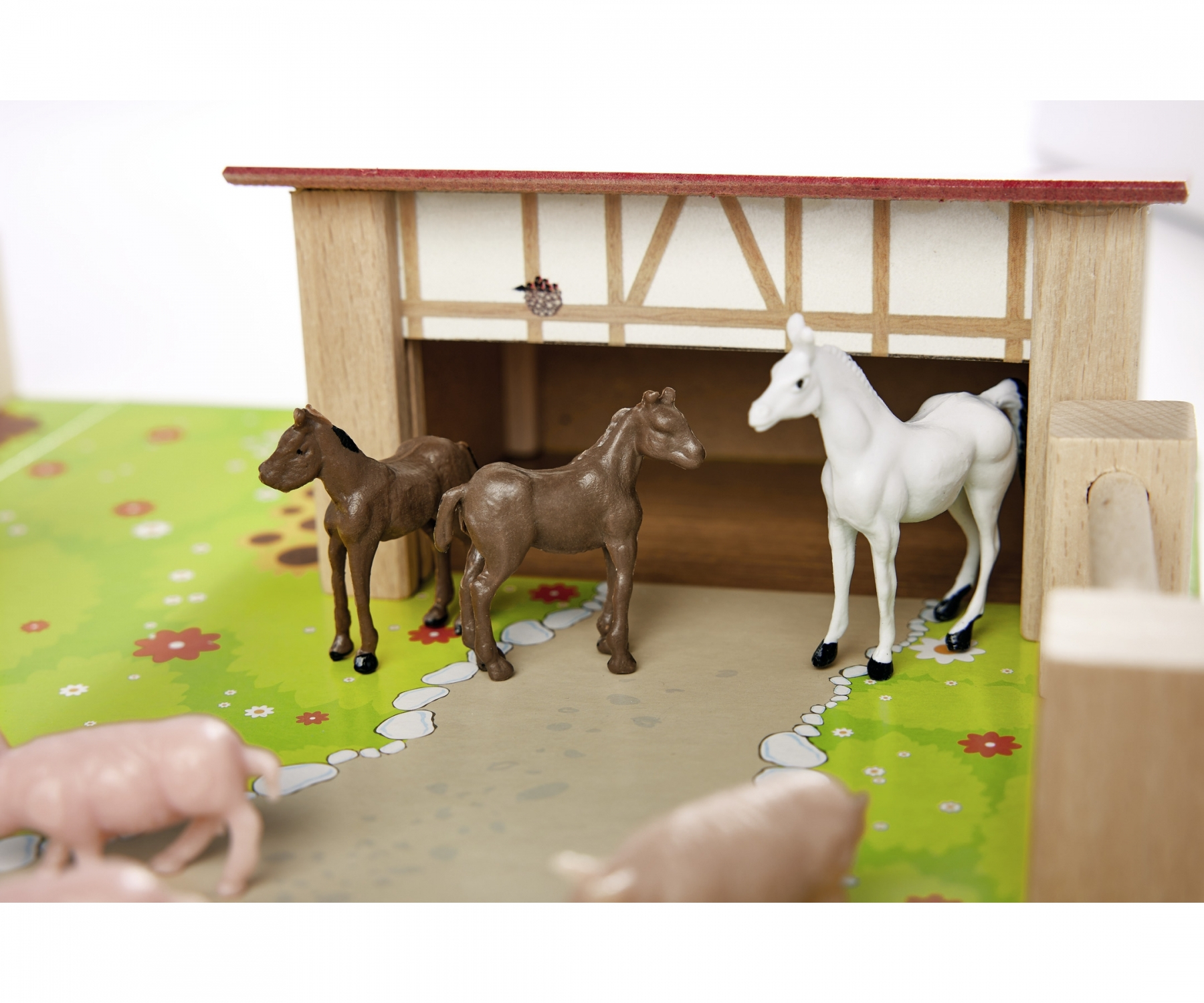 Scena z farmy z zabawkami z końmi przed stodołą. Zielona trawa i drewniane konstrukcje.