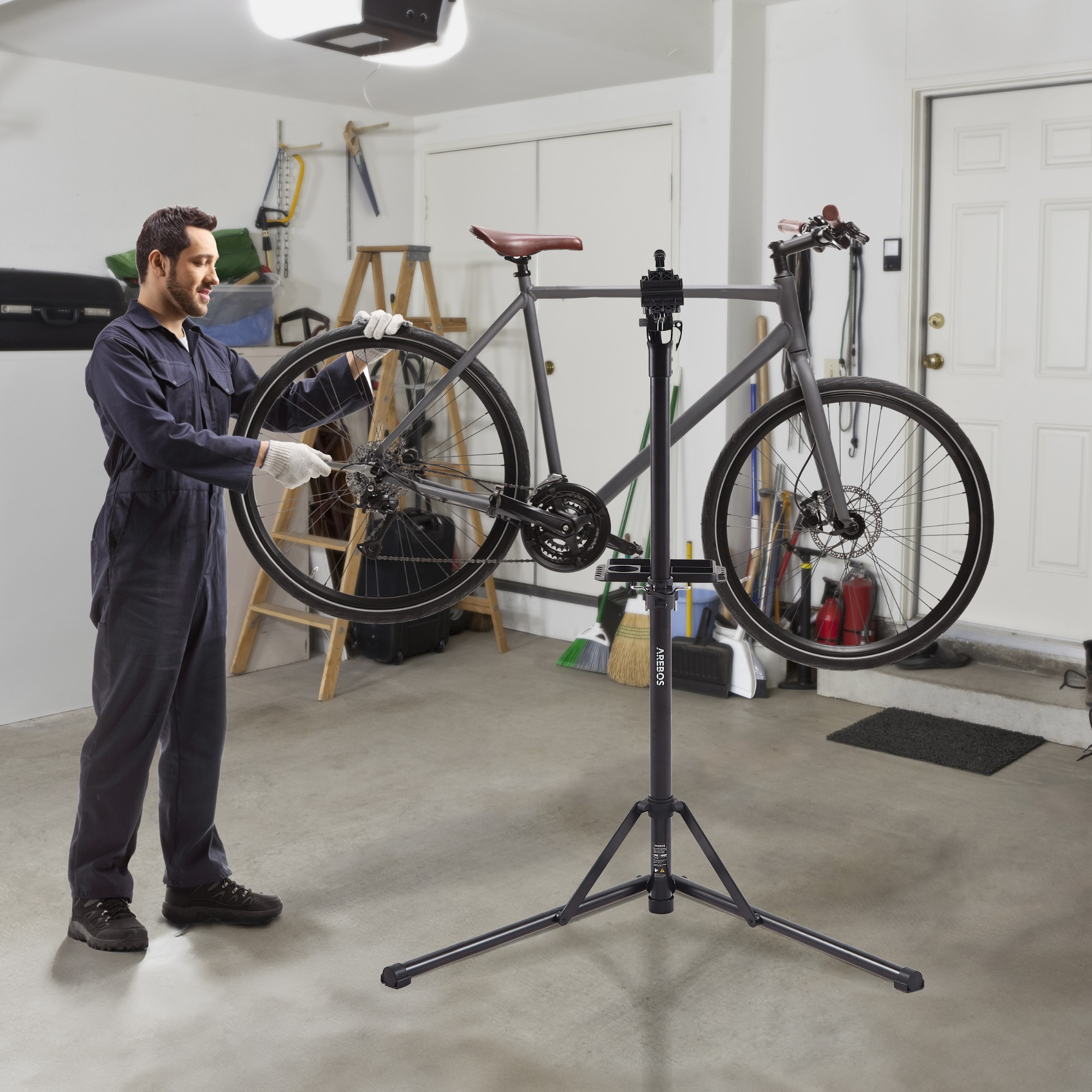 Ein Mann in einer Garage repariert ein Fahrrad auf einem Ständer. Das Fahrrad ist grau.