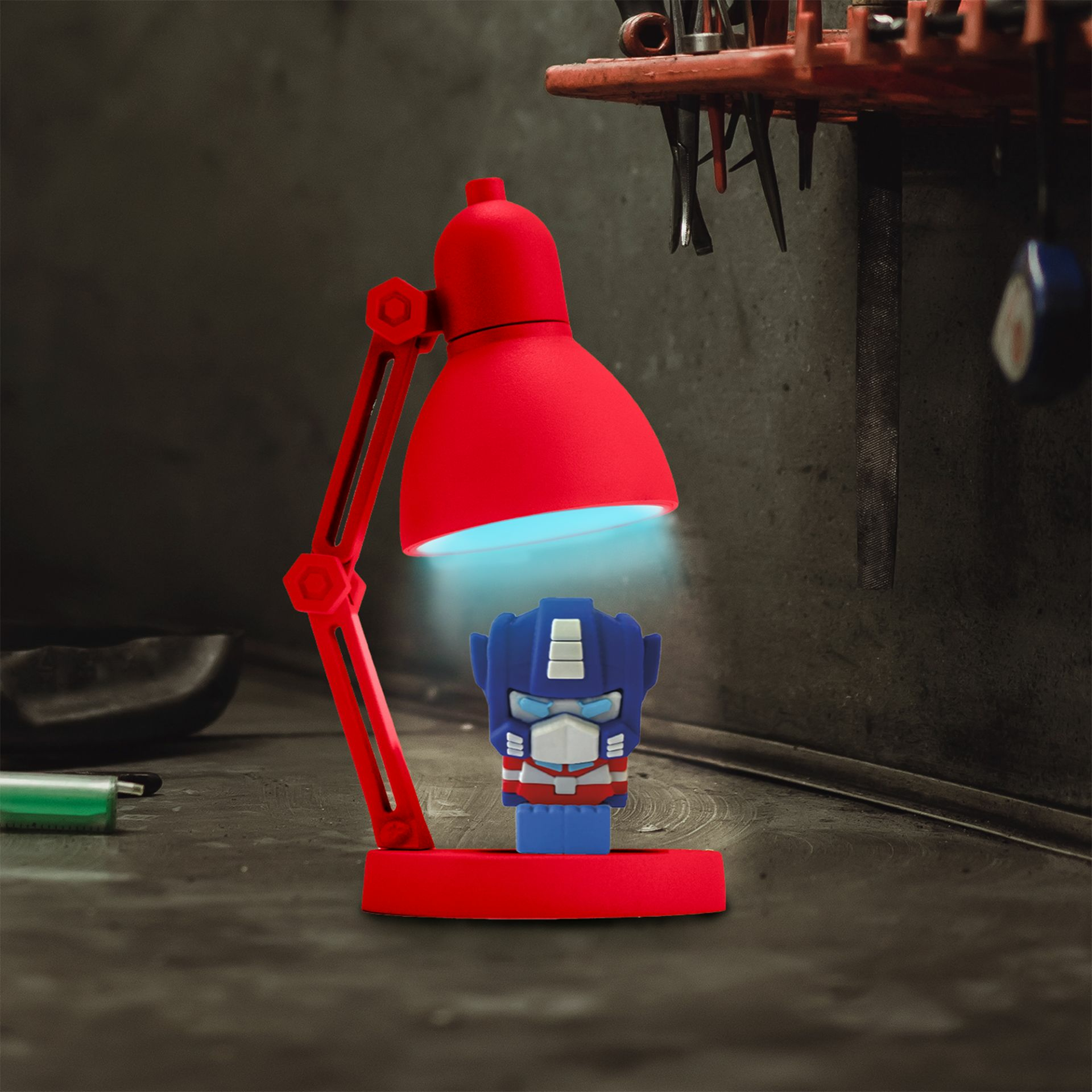 Eine rote Schreibtischlampe beleuchtet ein Optimus Prime-Spielzeug. Die Szene spielt in einer Werkstatt.