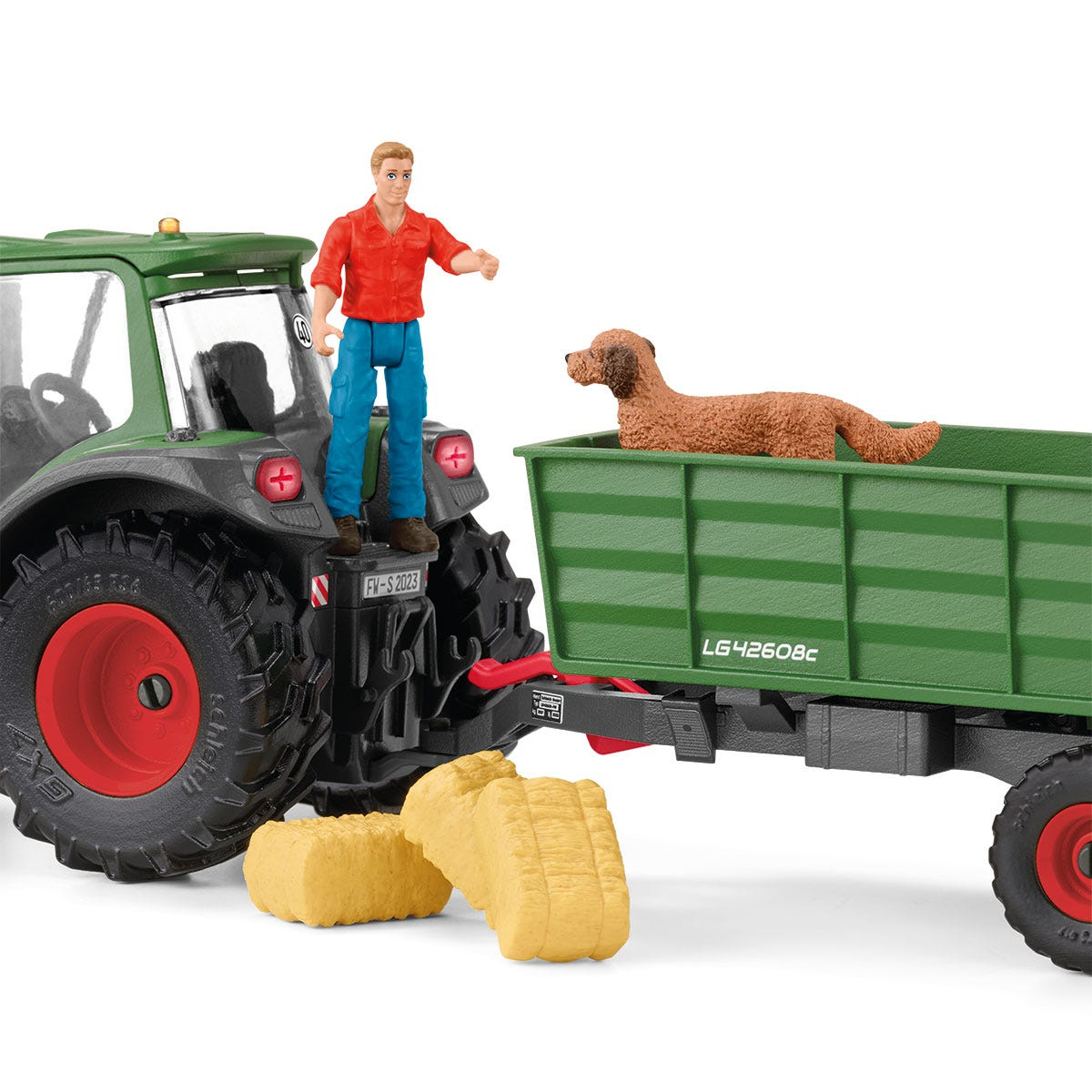 Ein grüner Traktor zieht einen Anhänger mit einem Hund. Ein Mann steht auf dem Traktor.