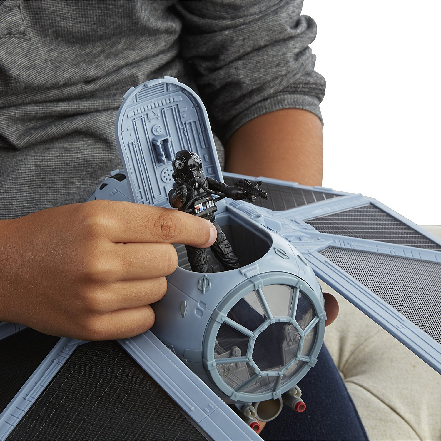 Kinderhände halten ein Star Wars TIE Fighter Spielzeug. Der Kämpfer ist grau mit schwarzen Details.