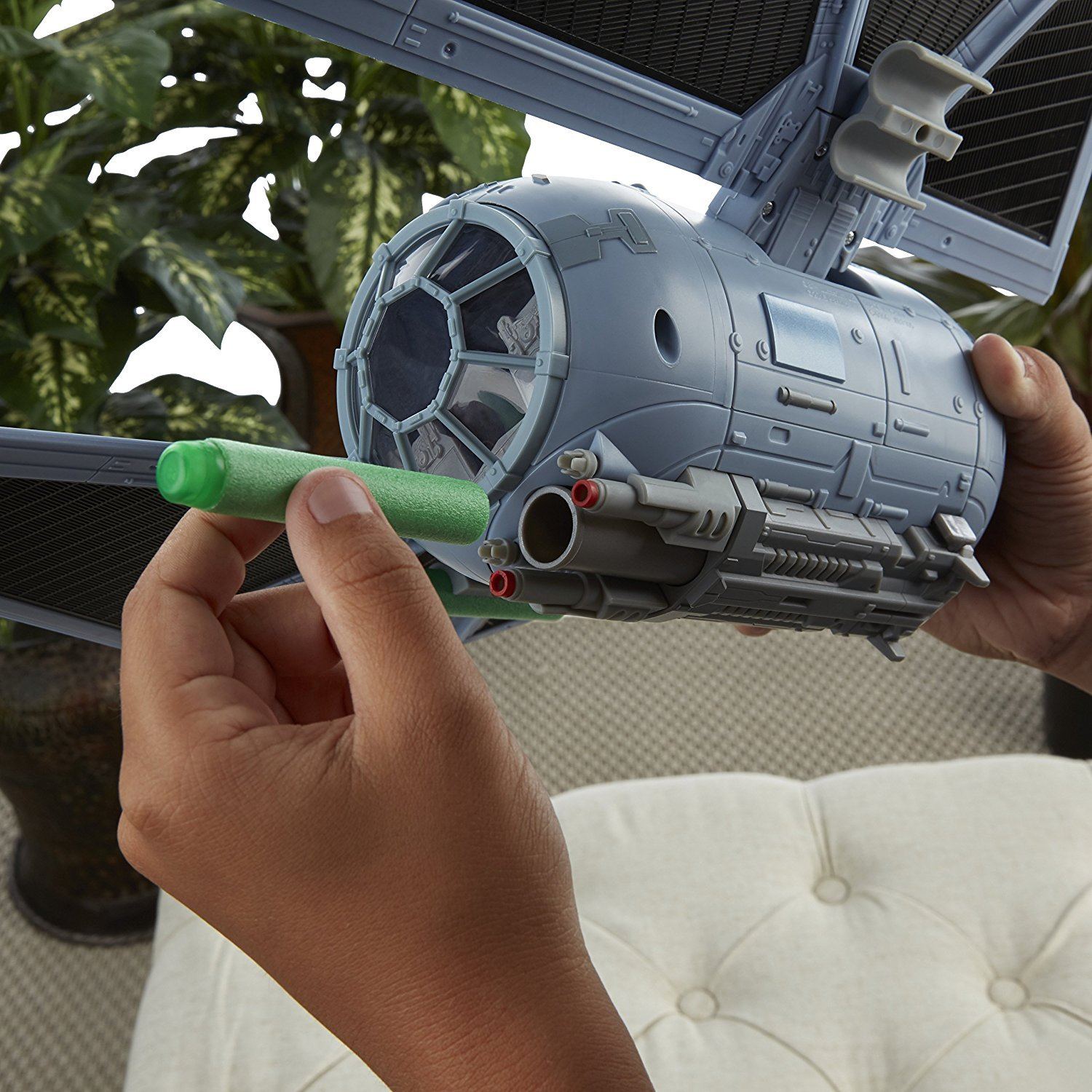 Hände halten ein graues TIE-Fighter-Spielzeug. Ein grünes Projektil wird in der Nähe der Kanone gehalten.