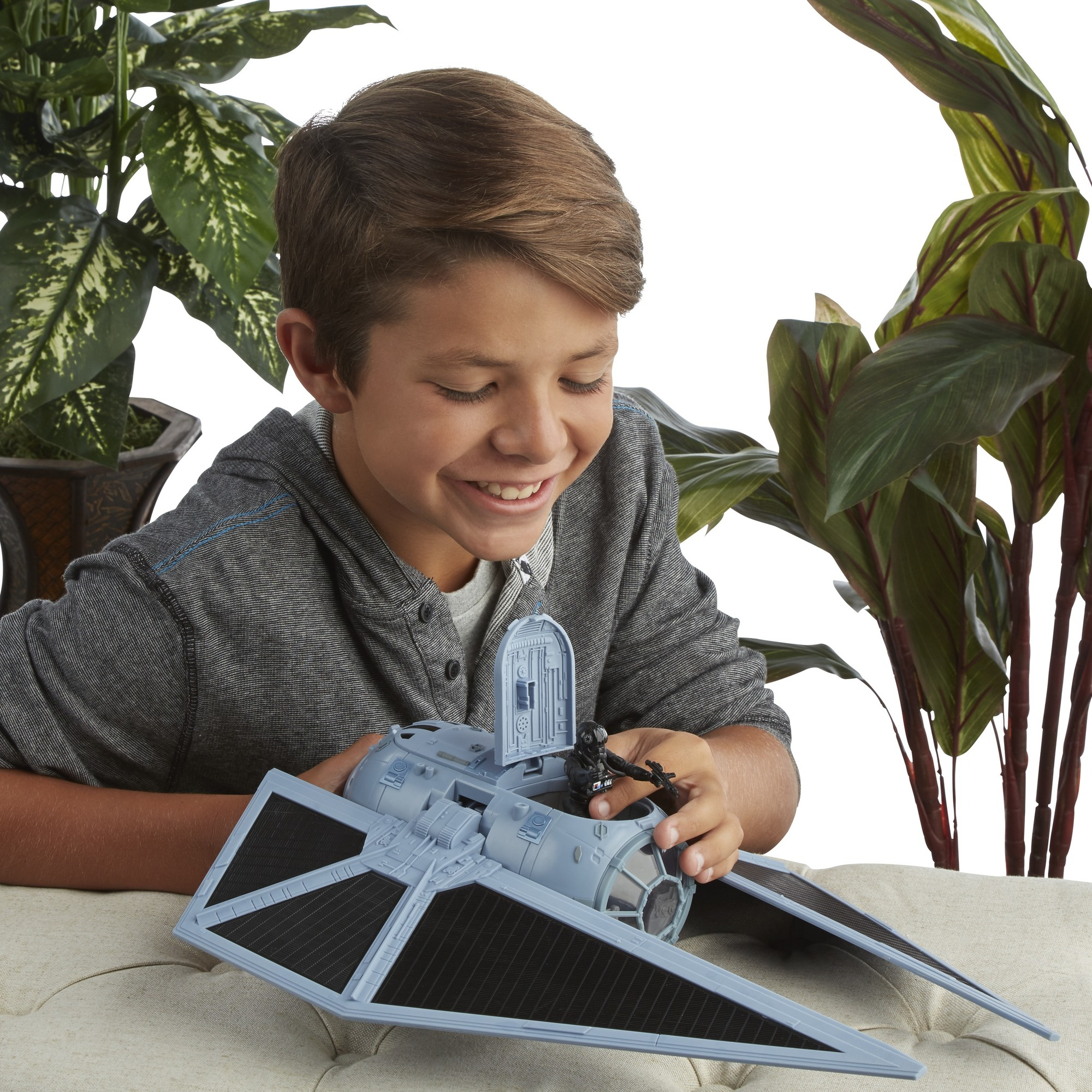 Junge spielt mit einem Star Wars TIE Fighter Spielzeug. Grüne Pflanzen sind im Hintergrund.