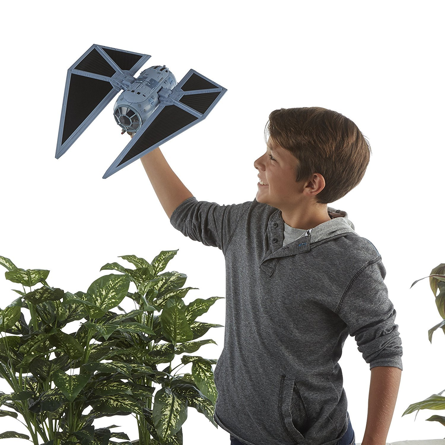Ein Junge hält ein Star Wars TIE Fighter Spielzeug. Grüne Pflanzen sind im Hintergrund.
