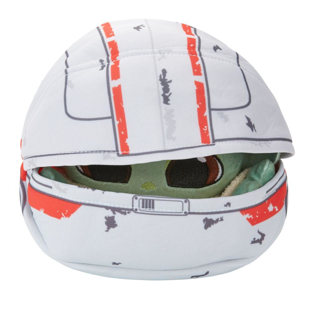 Peluche de Grogu dentro de un casco blanco y rojo con fondo gris y blanco.