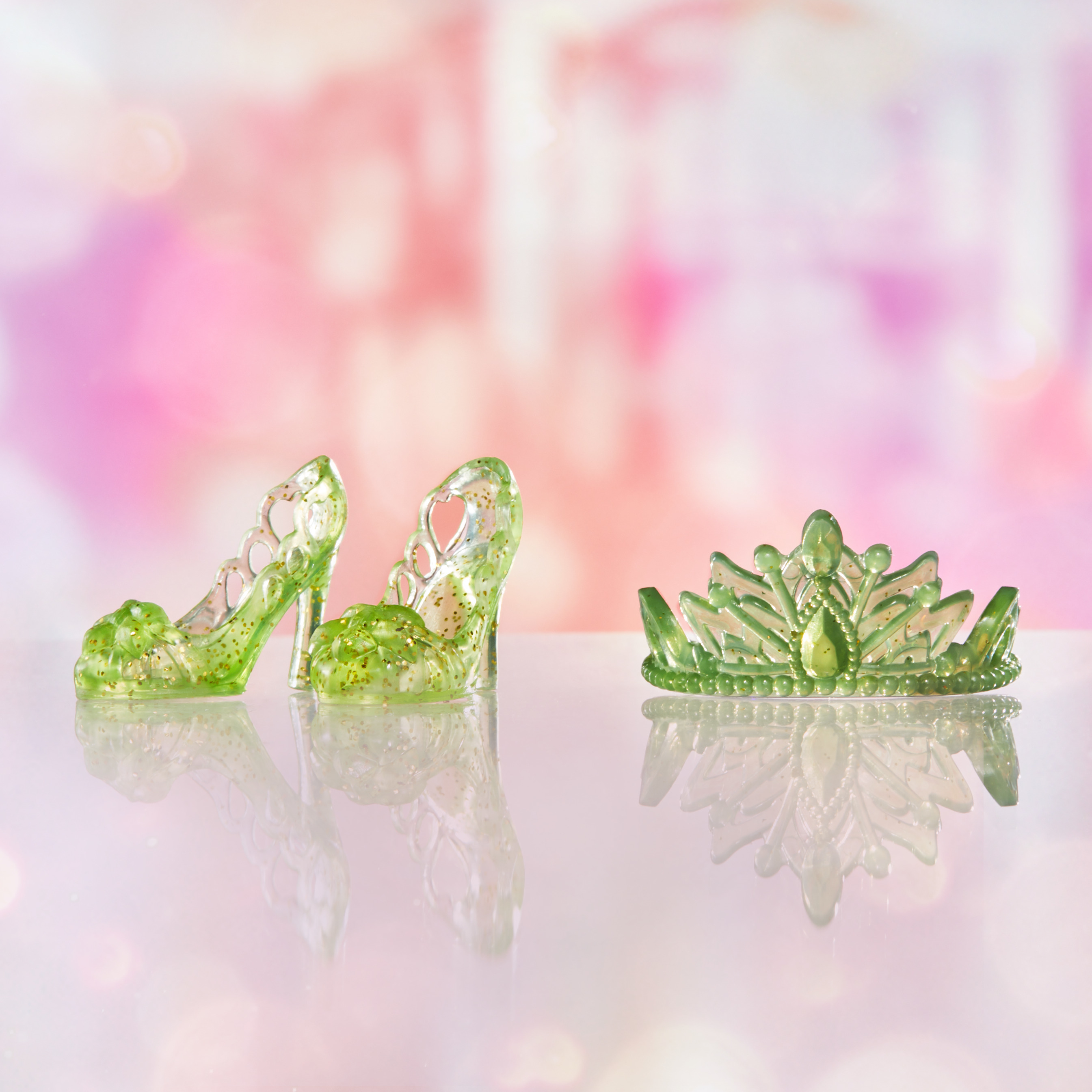 Tacchi alti verdi e una tiara verde con brillantini su una superficie riflettente e uno sfondo rosa.