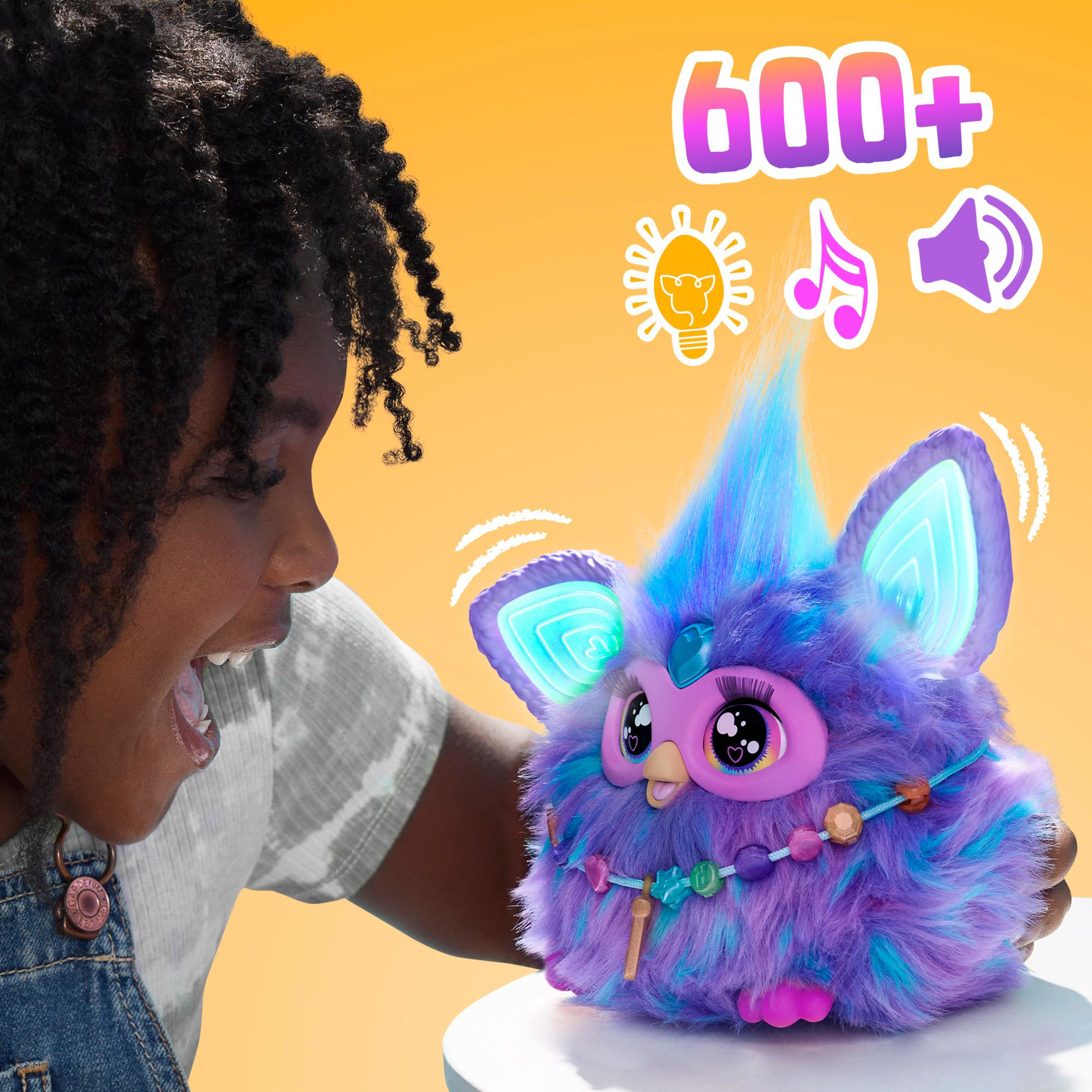 Ein Mädchen freut sich und betrachtet ein lila-blaues Furby-Spielzeug mit leuchtenden Ohren und Zierperlen.