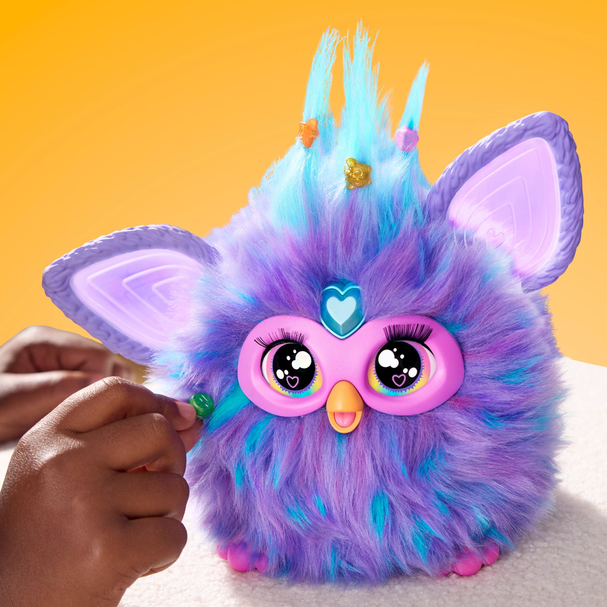 Furby-Spielzeug mit buntem Fell, eine Hand greift nach einer Dekoration.
