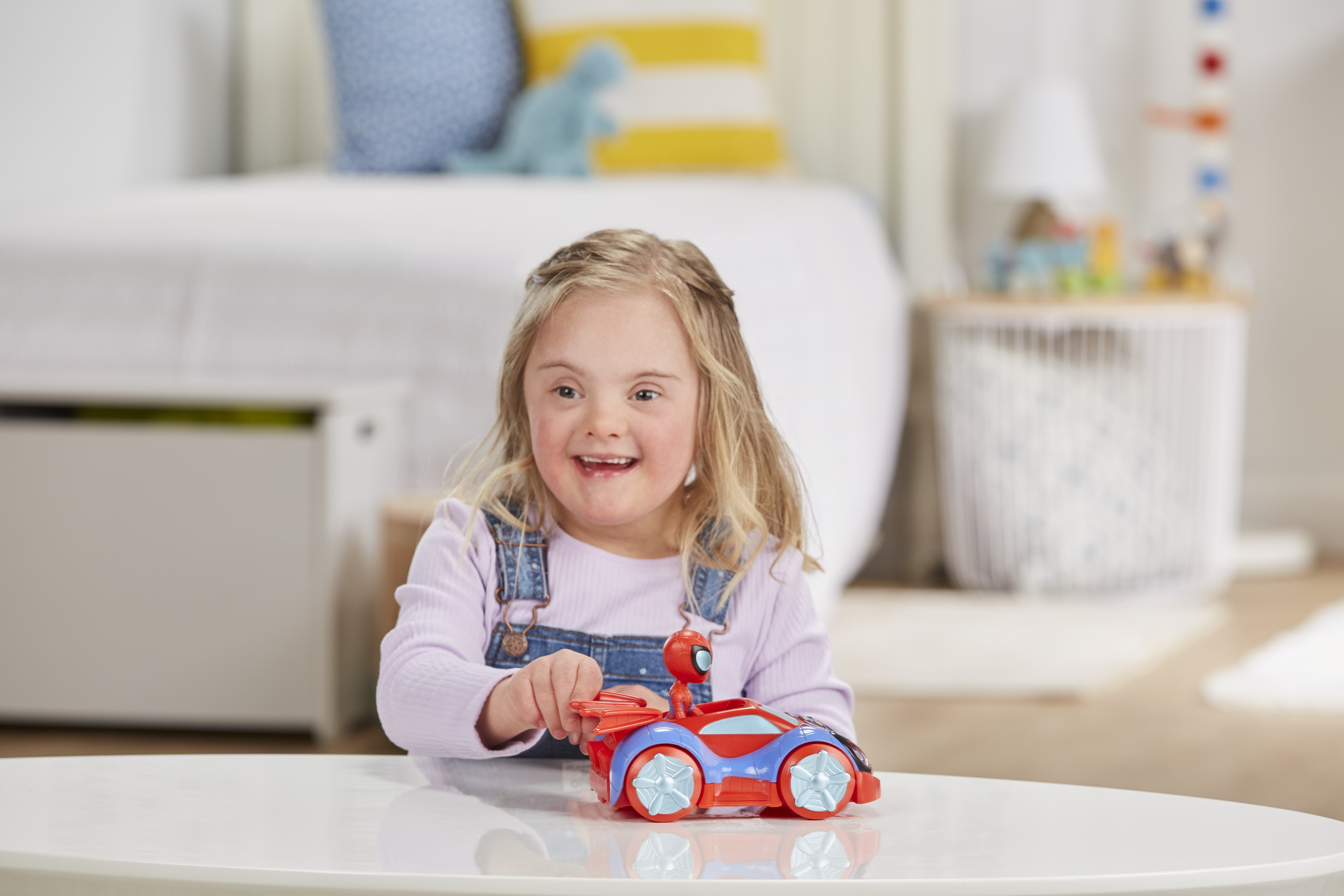 Dziewczynka z zespołem Downa uśmiecha się, bawiąc się czerwoną i niebieską zabawką-samochodem.
