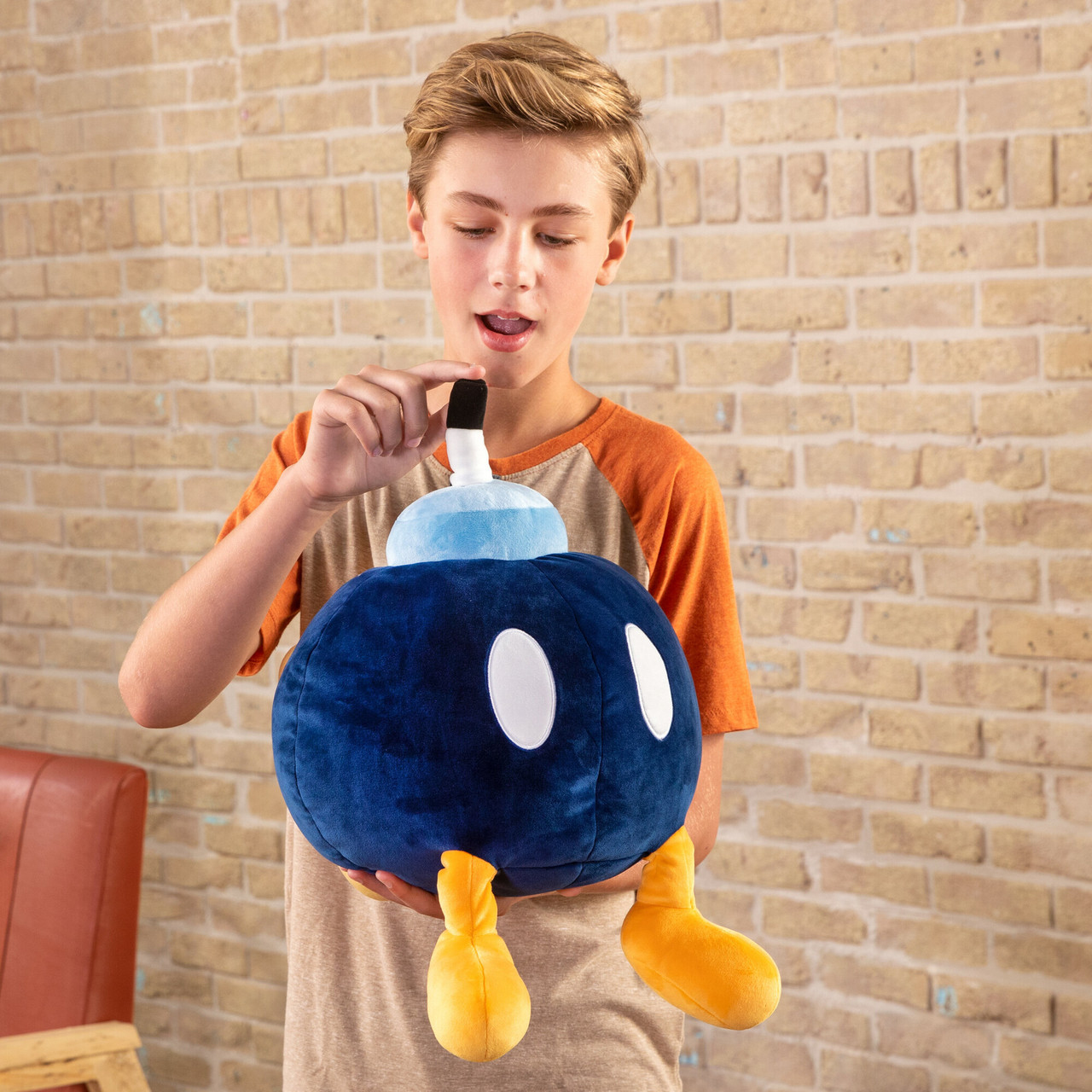 Un ragazzo che tiene in mano un grande peluche a forma di bomba blu con occhi bianchi e piedi gialli.