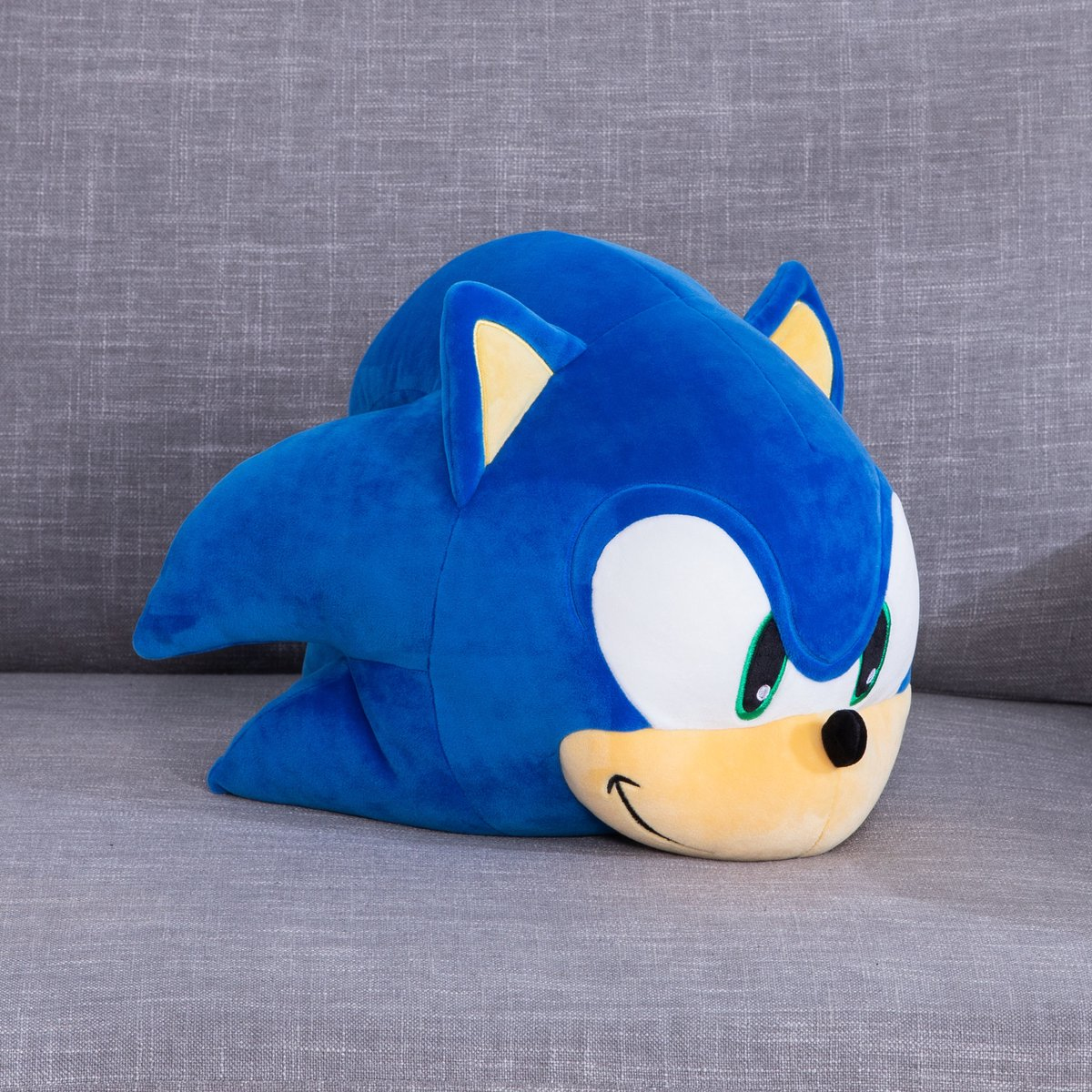 Un peluche di Sonic blu sdraiato su un divano grigio.