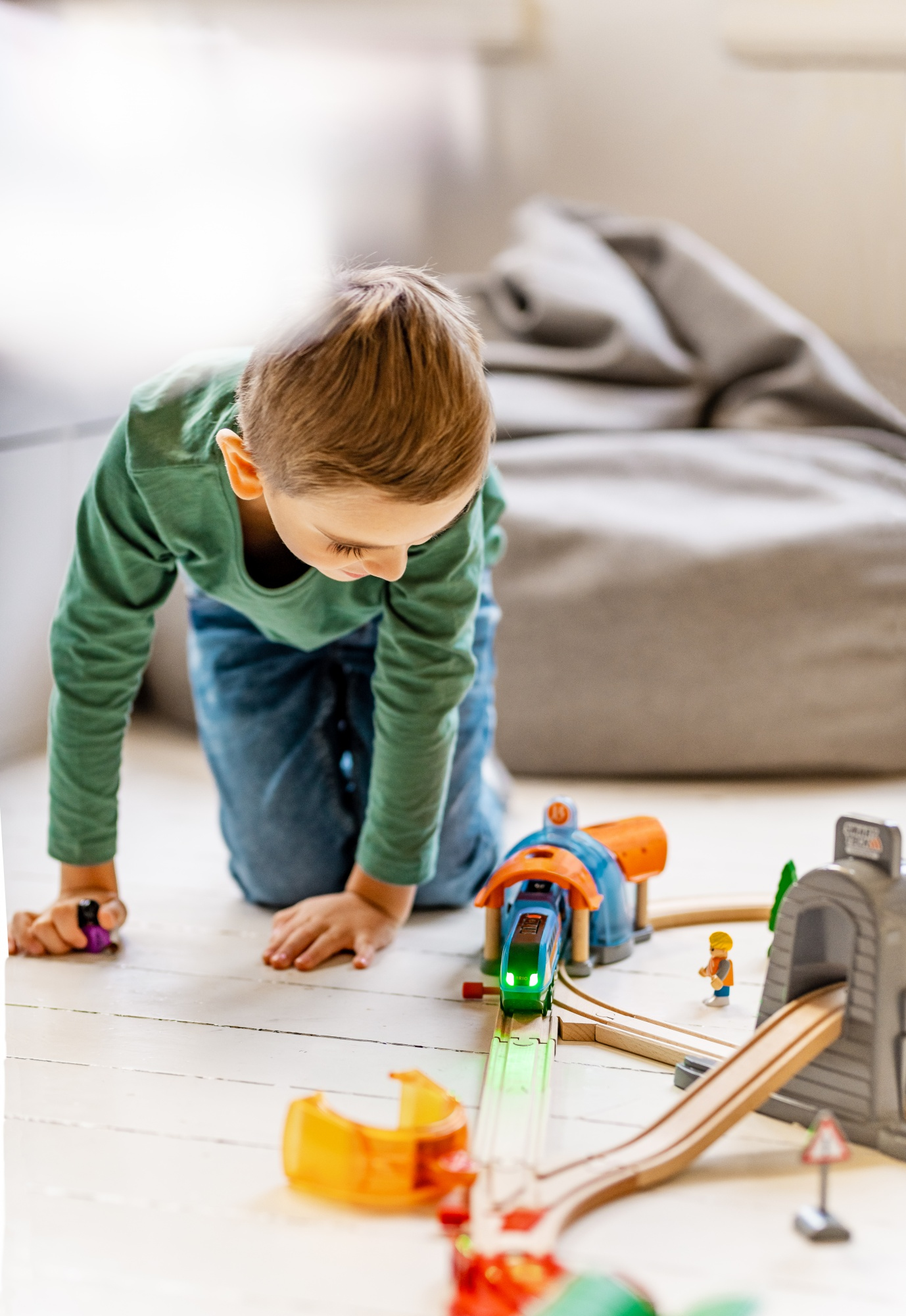 Ein kleiner Junge spielt mit einem Spielzeug-Eisenbahn-Set auf einem weißen Boden. Bahngleise und anderes Spielzeug sind sichtbar.