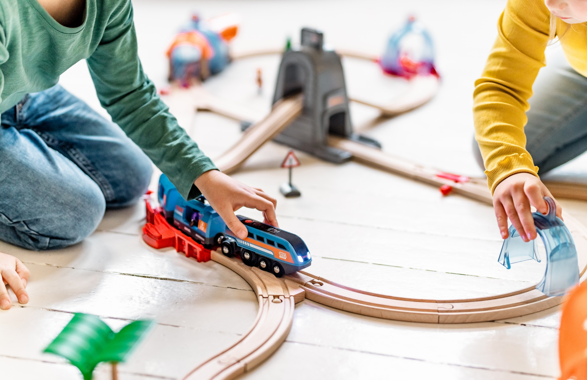 Zwei Kinder spielen mit einer Holzeisenbahn. Ein Zug fährt auf den Gleisen mit Brücken und Tunneln.