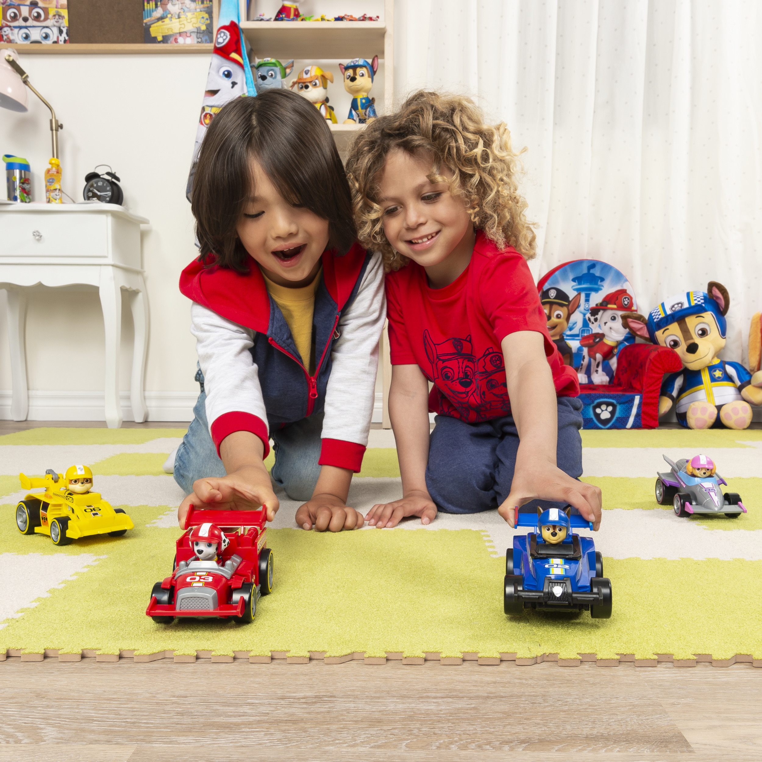 Dwoje dzieci bawiących się samochodzikami na zielono-żółtej macie w wzory.