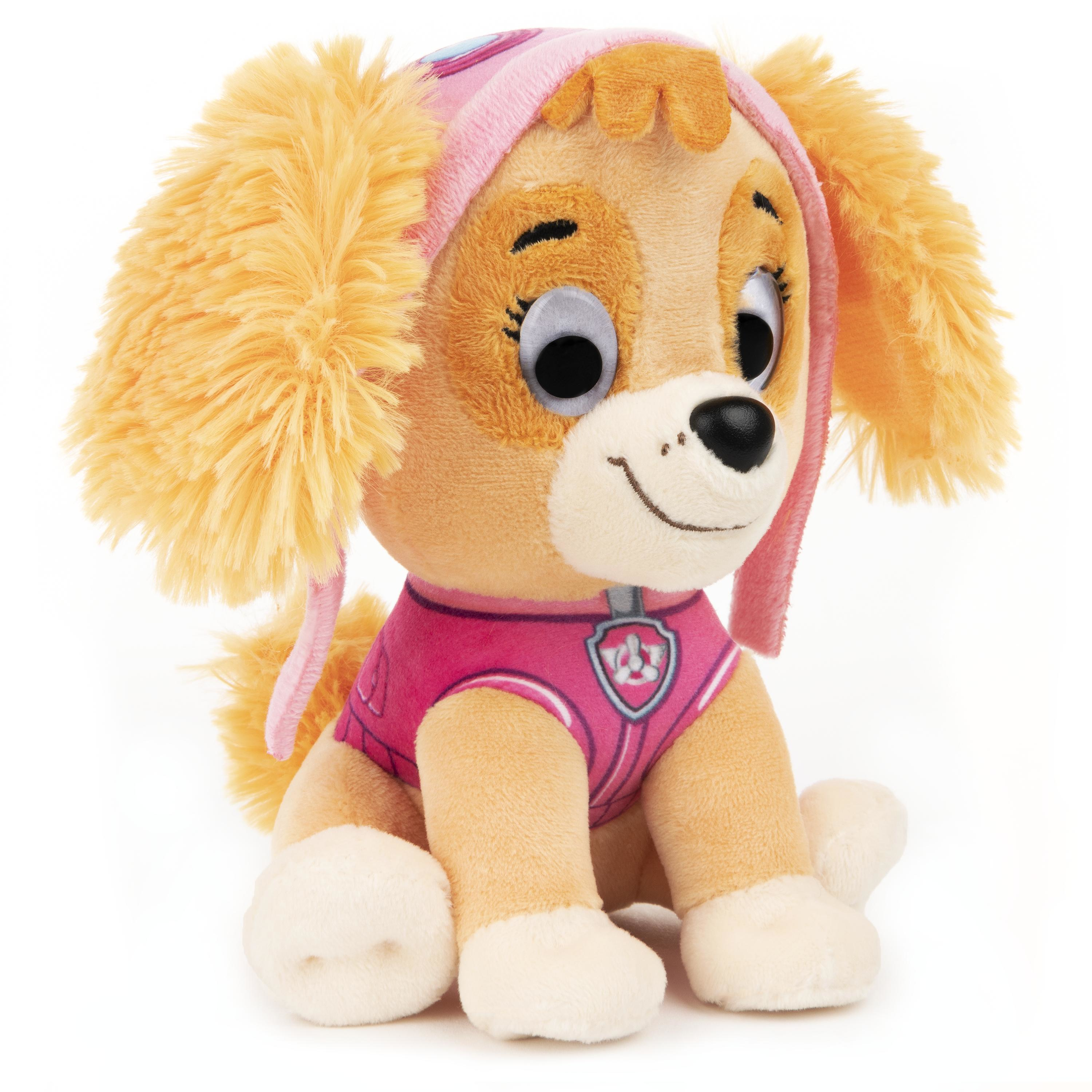 Skye, ein Stofftier-Welpe von Paw Patrol, trägt ein rosa Outfit und einen Hut und sitzt auf einer weißen Oberfläche.