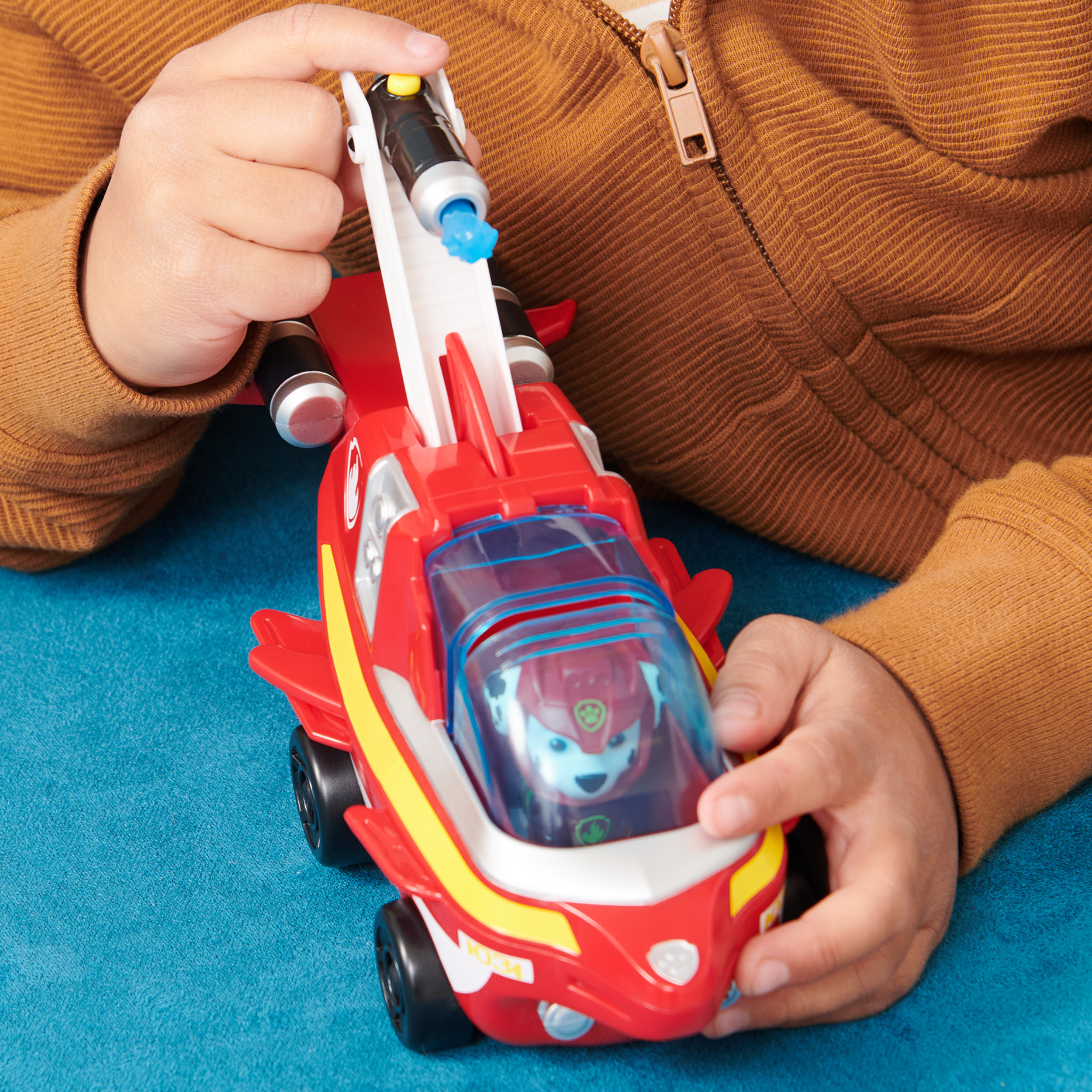 Mani di bambino che tengono un aereo giocattolo Paw Patrol rosso e bianco con un personaggio dentro.