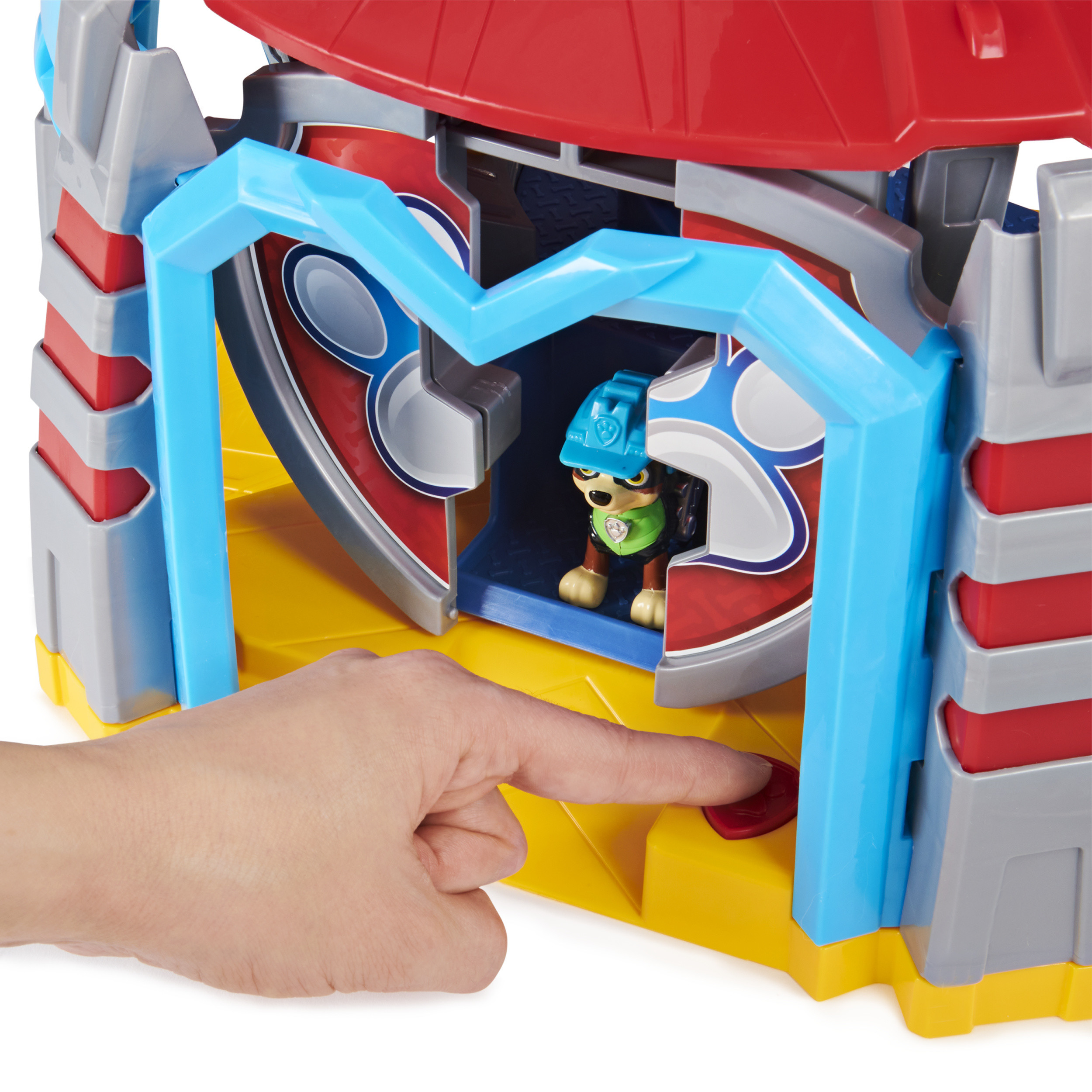 Un juego de juguetes de Paw Patrol. El dedo de un niño presiona un botón rojo. Un personaje de perro es visible dentro.