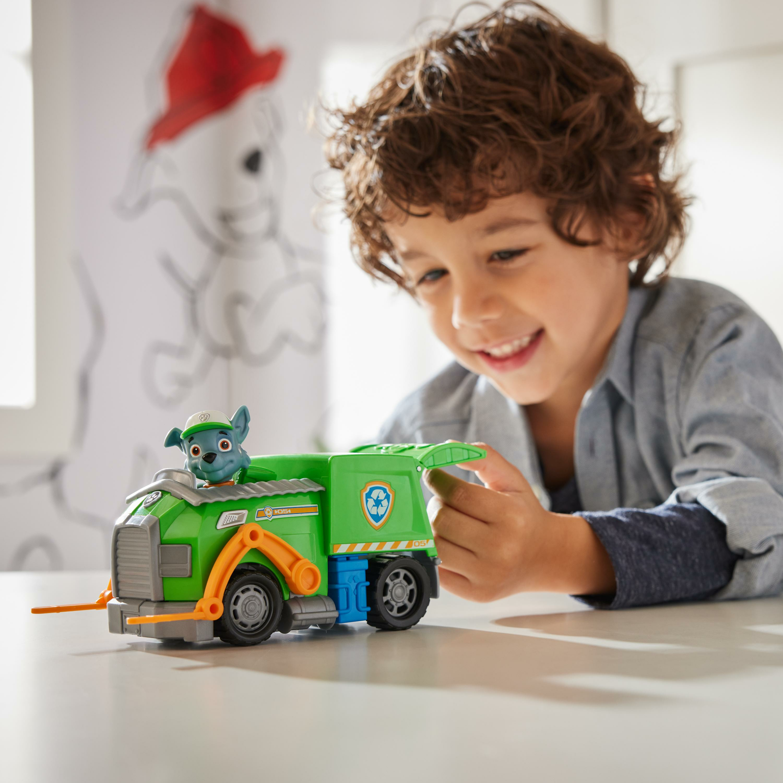 Ein Junge spielt mit einem grünen Spielzeug-Müllwagen, mit einer Zeichnung im Hintergrund.