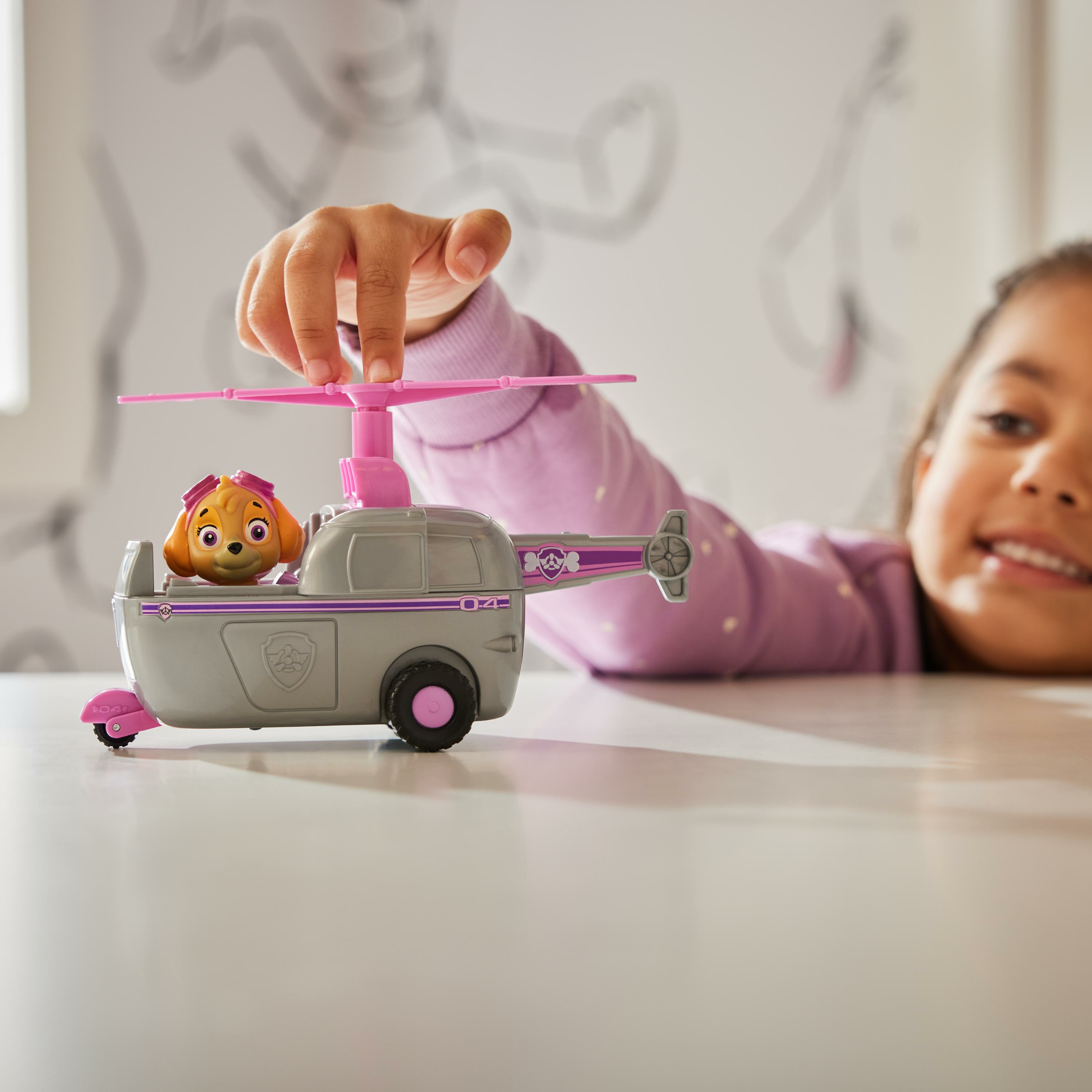 Kind spielt mit einem Spielzeug-Paw Patrol-Hubschrauber. Der Hubschrauber hat Skye drin.