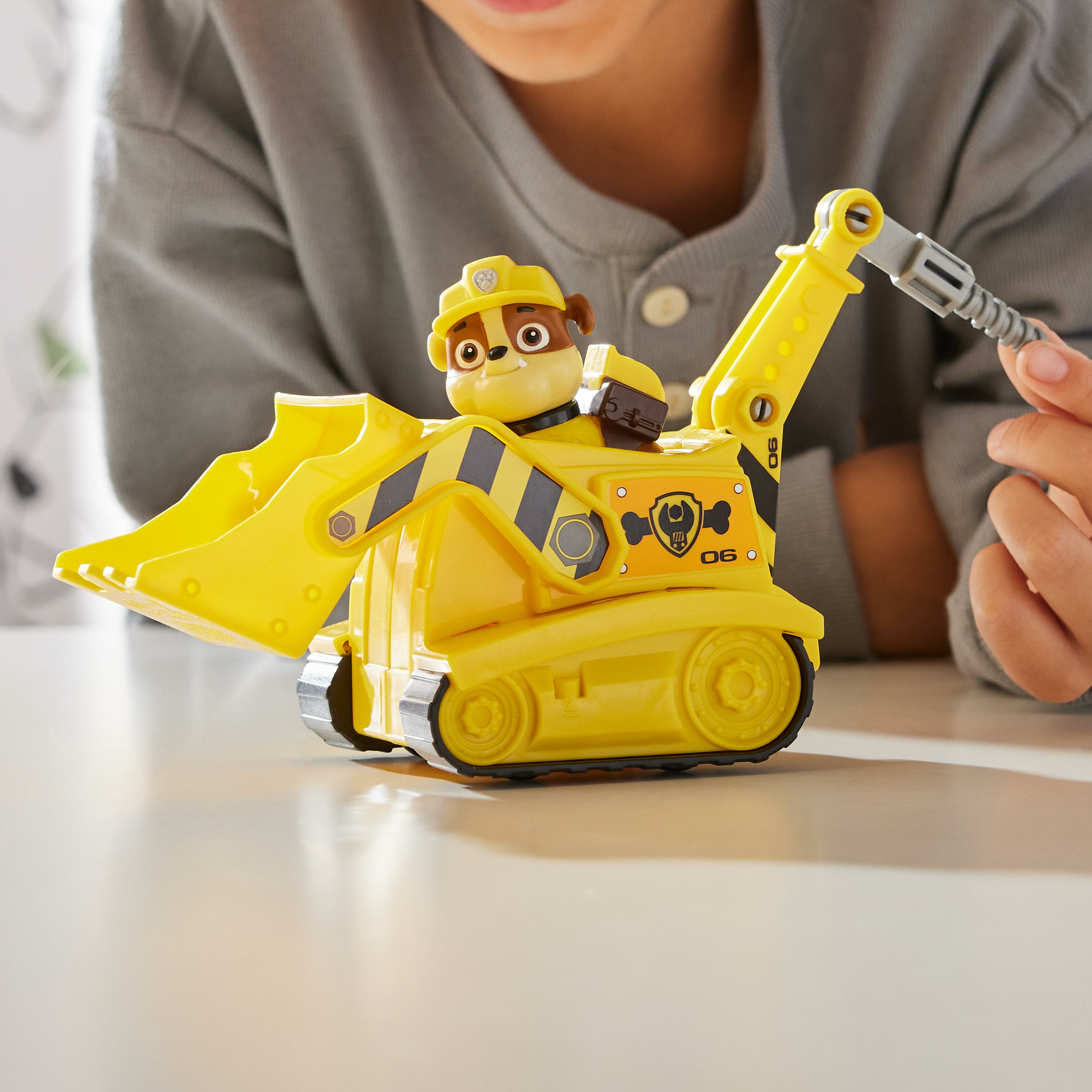 Kind spielt mit gelbem Paw Patrol Bulldozerspielzeug. Das Spielzeug hat eine Welpenfigur.