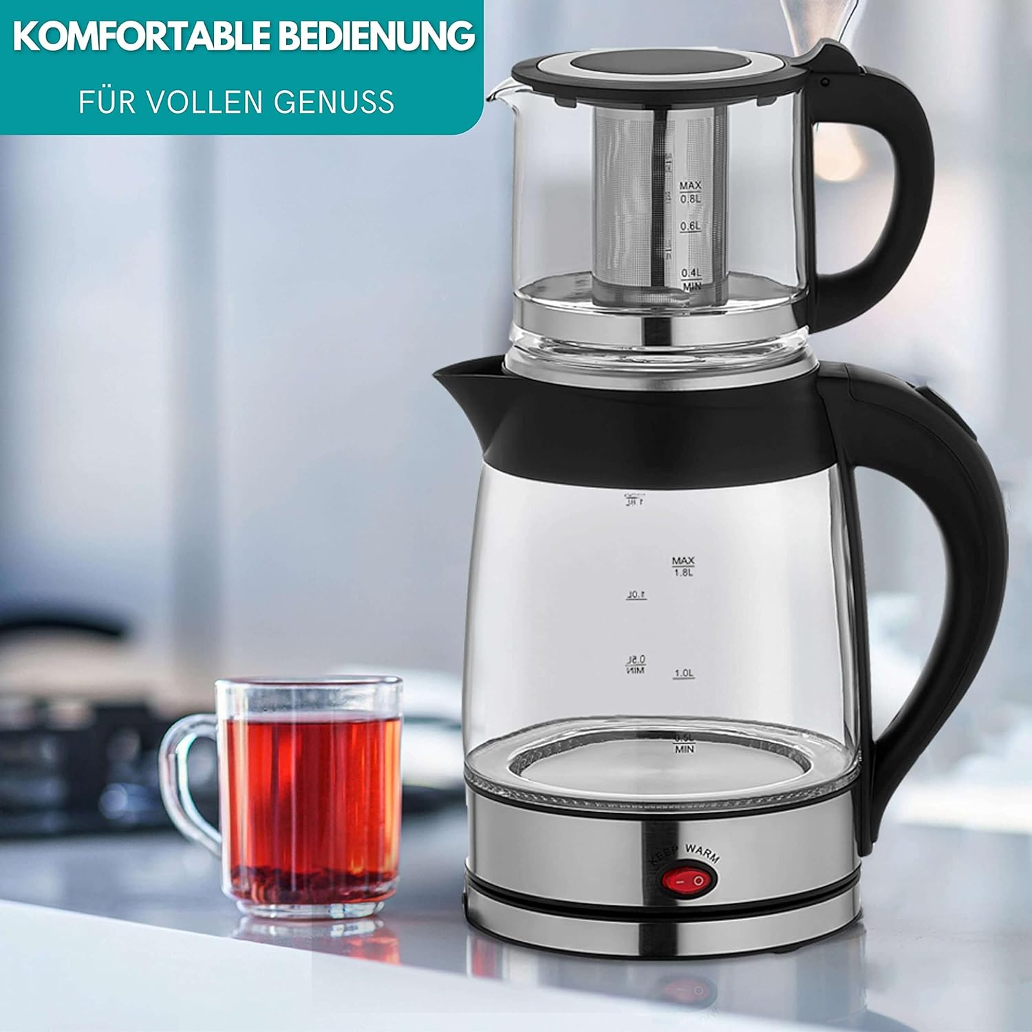 Gläserner Teezubereiter mit Tee-Infuser. Eine Tasse Tee daneben. Schwarzer Griff.