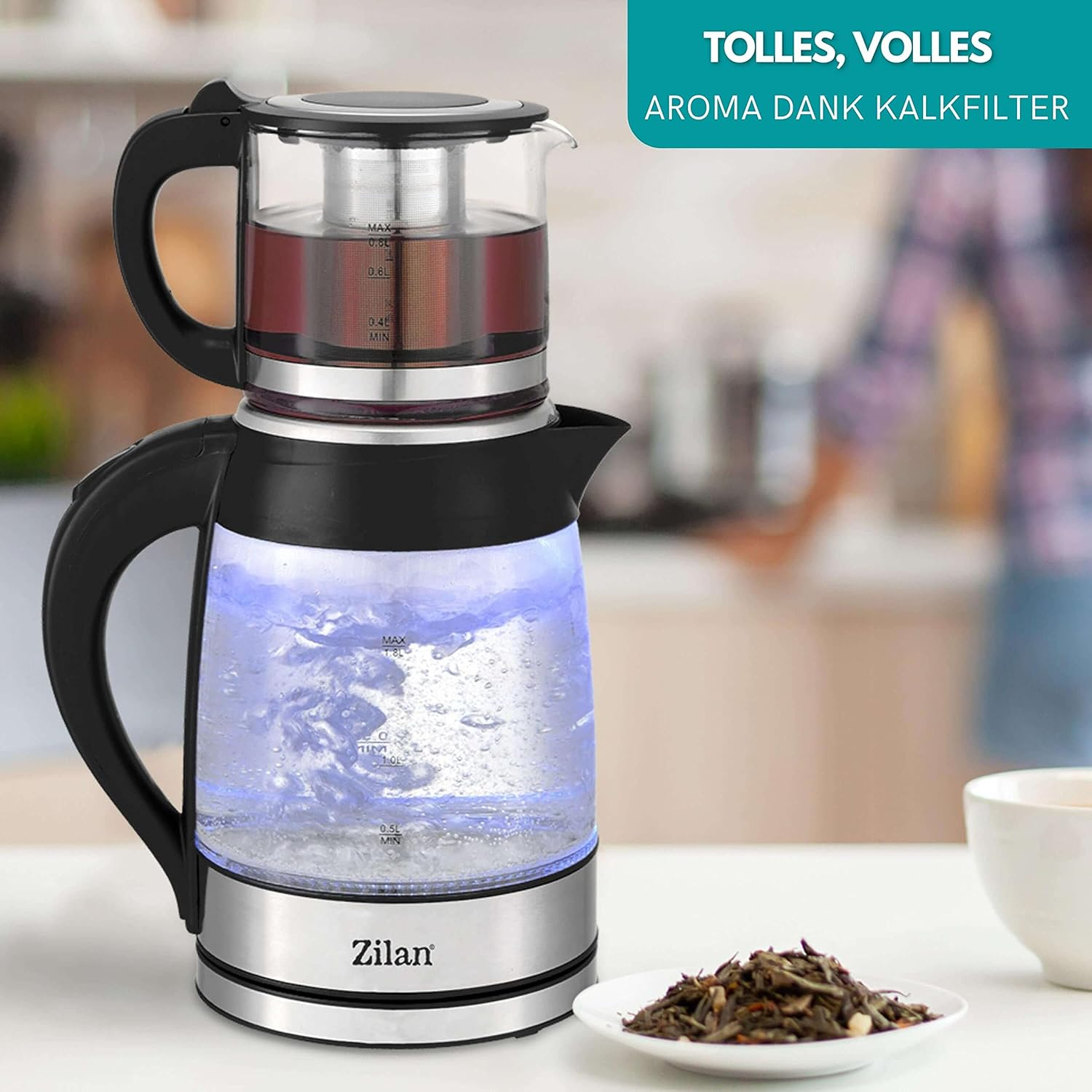 Ein gläserner Teekessel mit blauen Lichtern im Inneren. Teeblätter und eine Tasse sind in der Nähe.